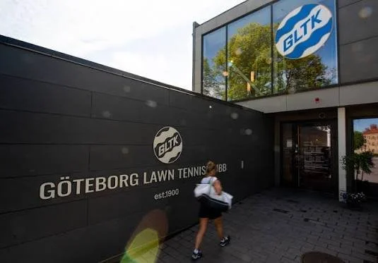 Person som går ut från göteborgs lawn tennis klubb utanför en svart vägg med Göteborgs Lawn Tennis klubb logga.