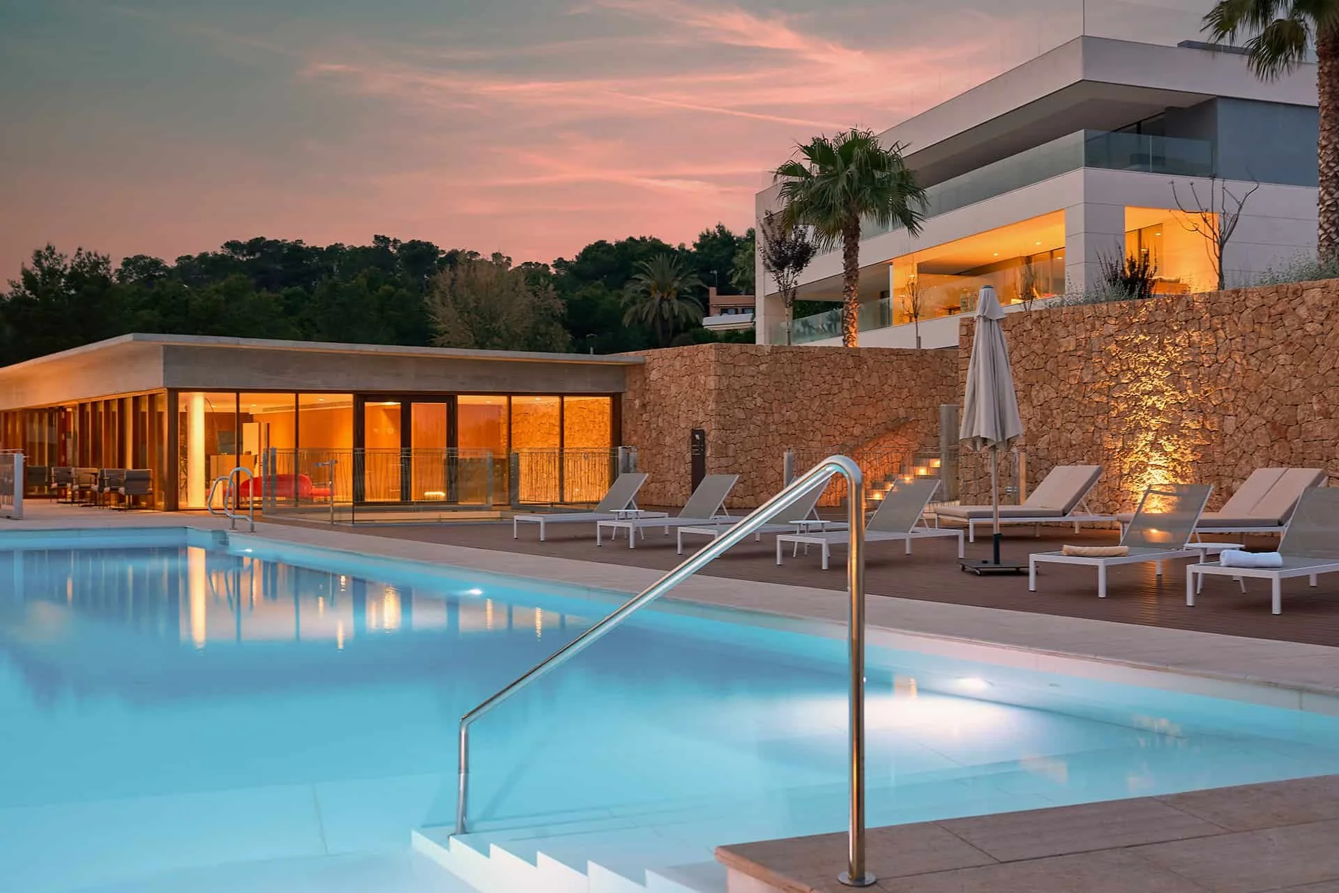 Piscina al atardecer con arquitectura contemporánea y muro de piedra en Cala Comte, vivienda residencial en Ibiza