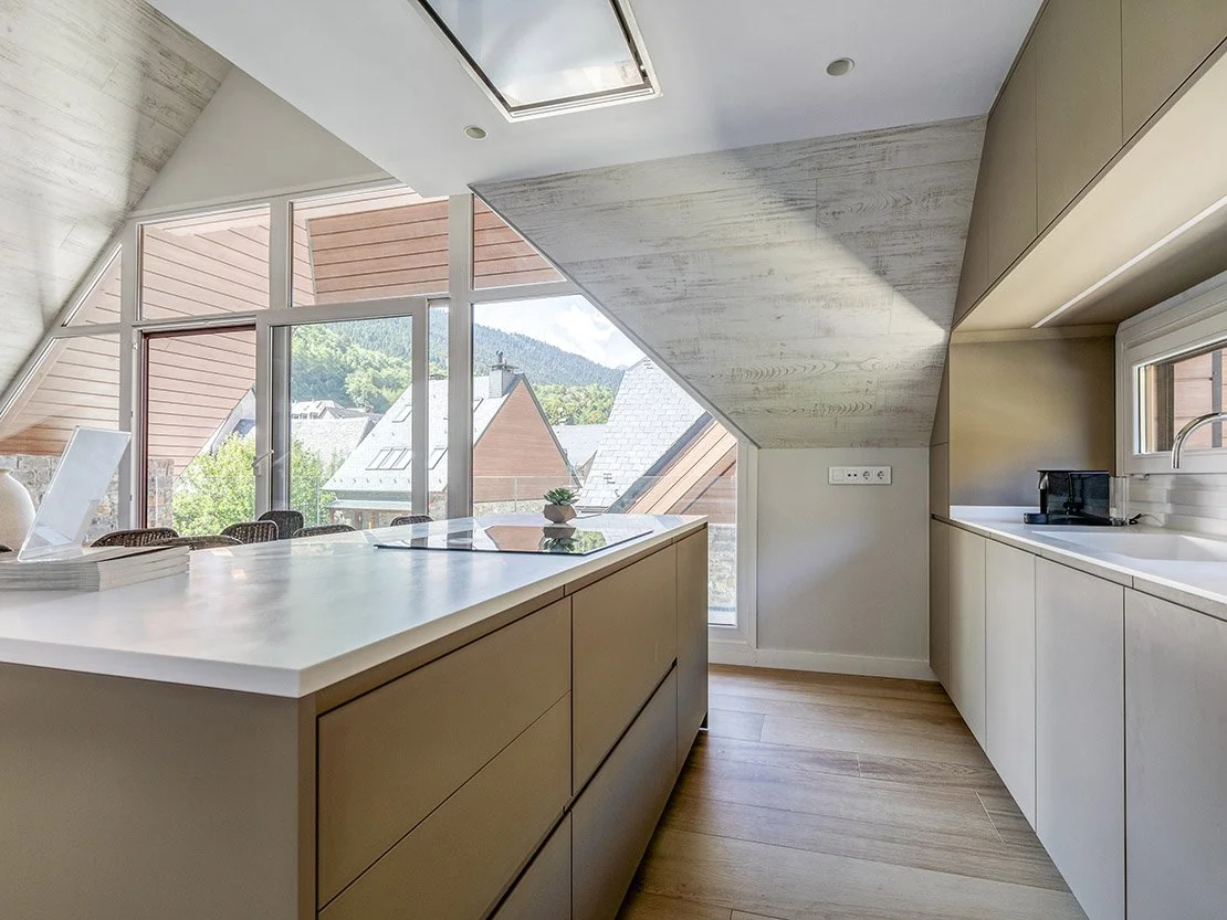 Cocina abuhardillada de Residencial Els Pletieus con isla central y vistas a los tejados de pizarra y las montañas