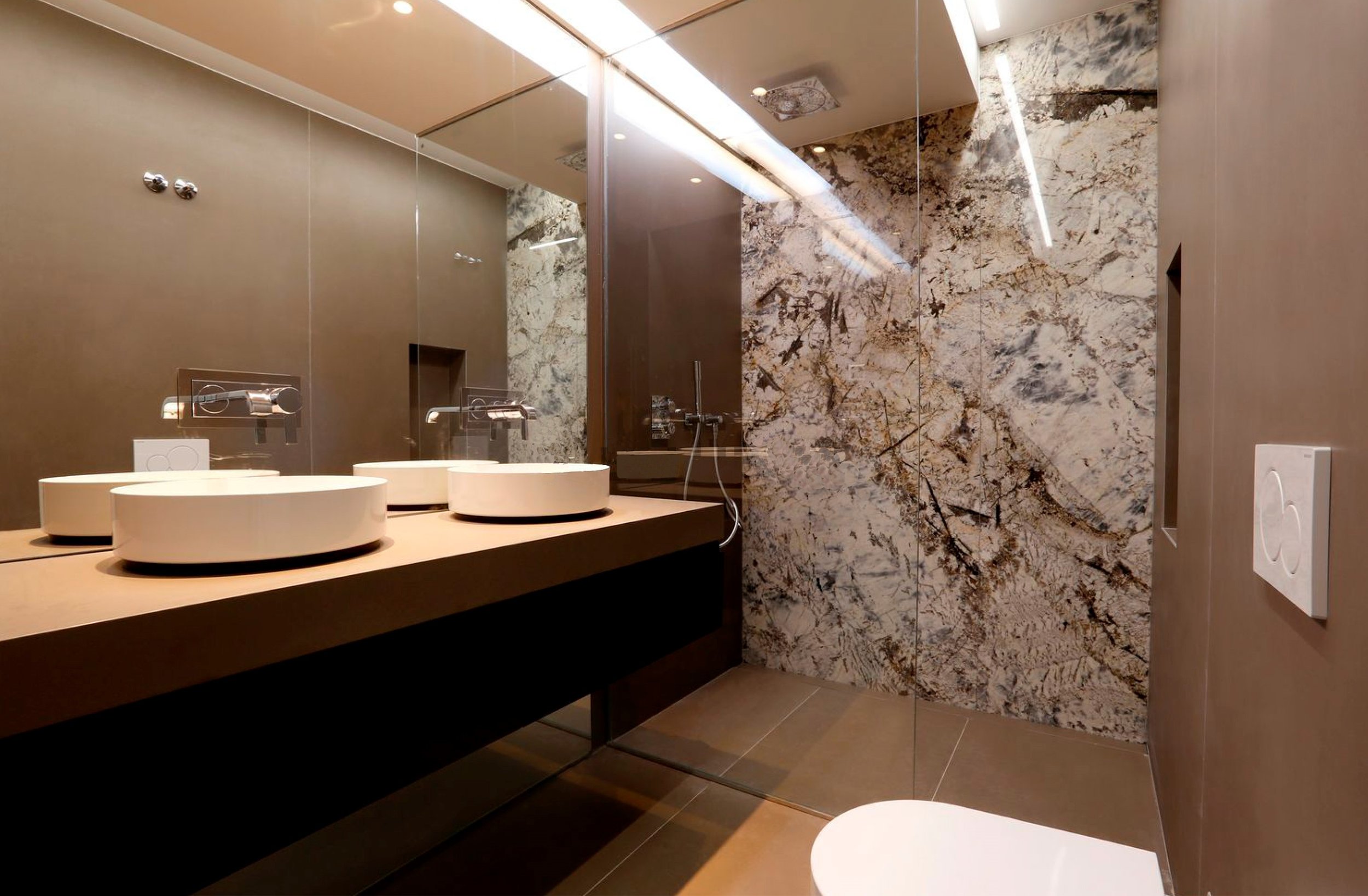 Baño de Pilar 14 con doble lavabo circular, mampara de cristal y pared de mármol veteado en la ducha