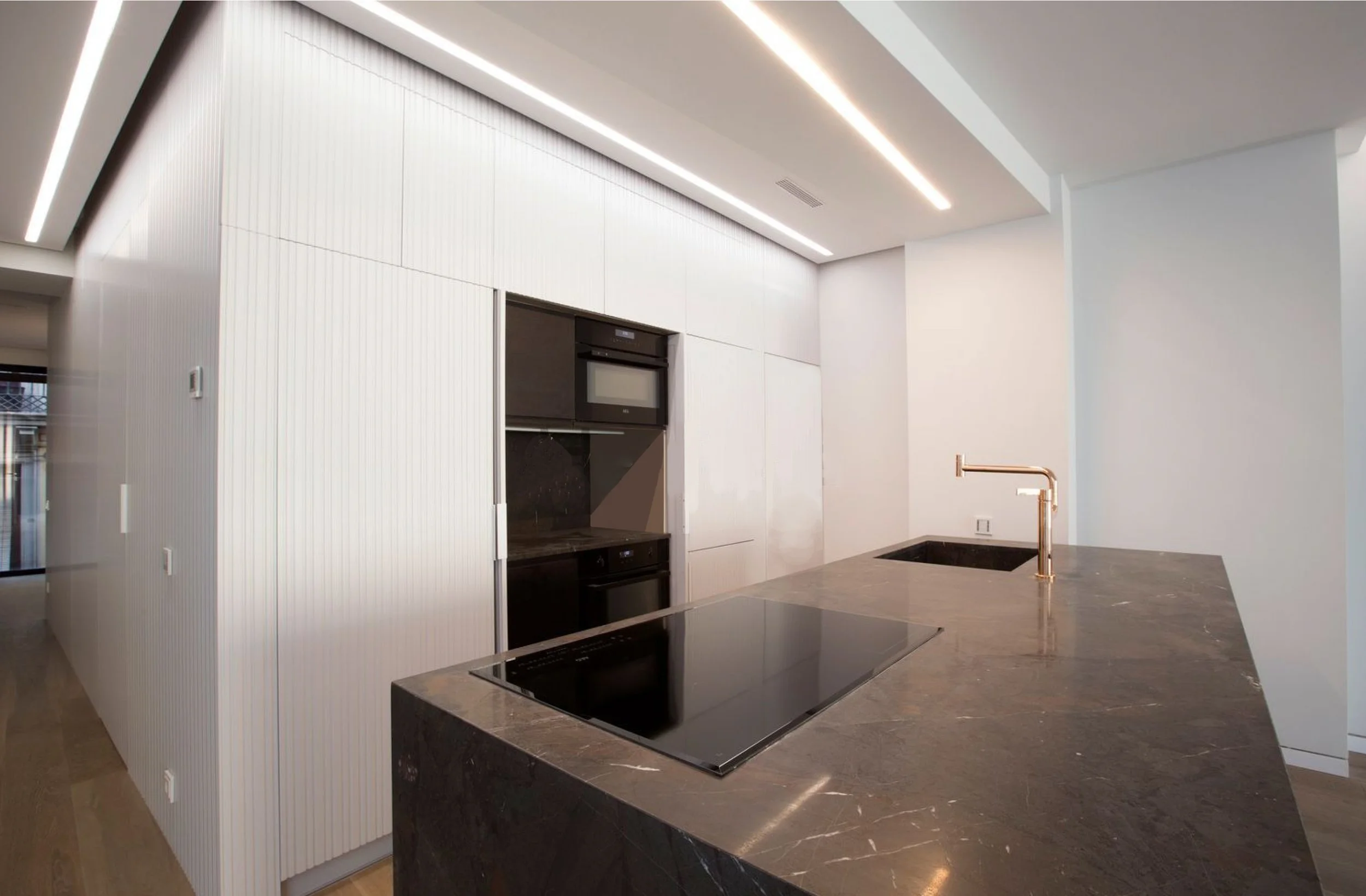 Cocina de Pilar 14 con isla de piedra negra veteada, grifería dorada y armarios blancos con luz LED integrada