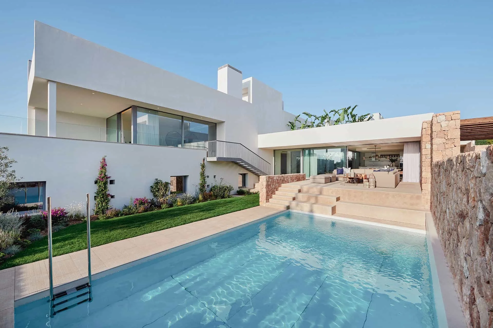 Piscina y jardín de Cala Comte, con fachada blanca contemporánea y salón abierto a la terraza a través de puertas acristaladas