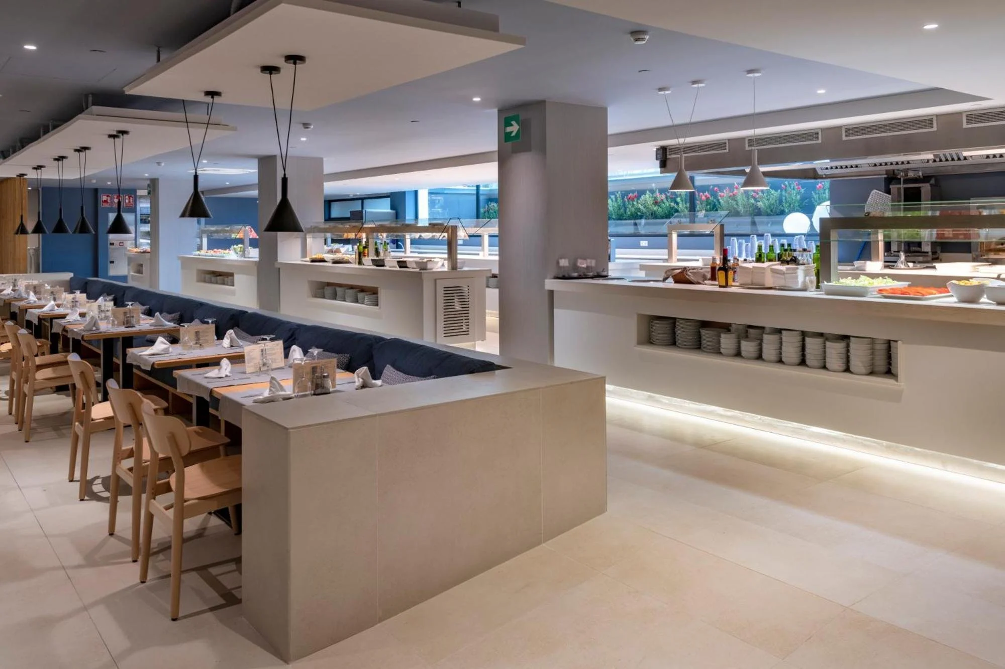 Comedor y zona de buffet de Caprici Beach Hotel & Spa, con bancos tapizados en azul y vistas al jardín