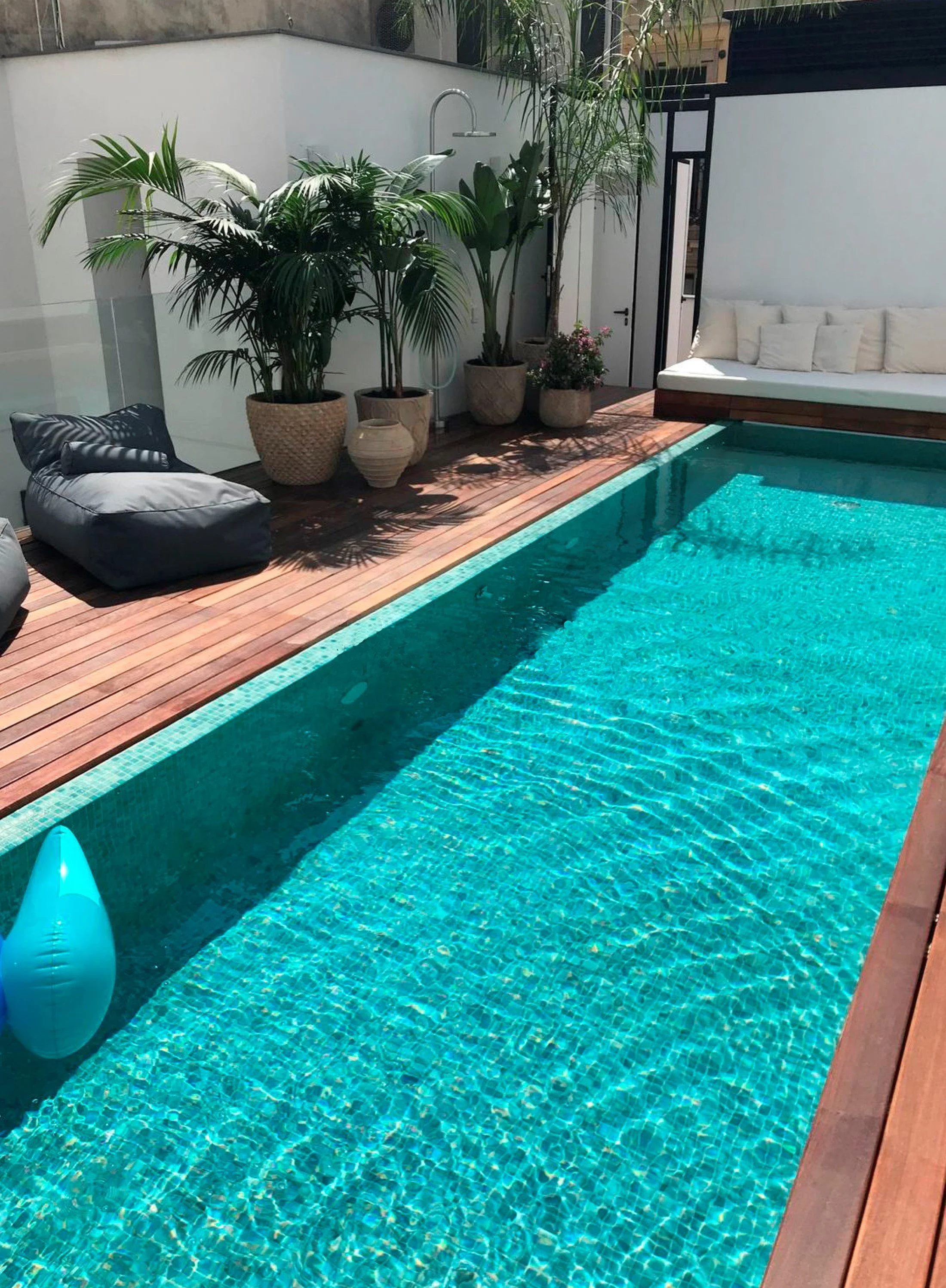 Piscina en la terraza de Pilar 14, con tarima de madera, plantas tropicales y zona de descanso junto al agua