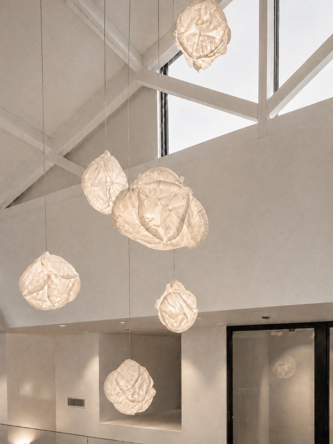 Composición de lámparas colgantes de papel plegado con forma de nube, suspendidas a distintas alturas bajo cubierta a dos aguas — solución de iluminación ZONA