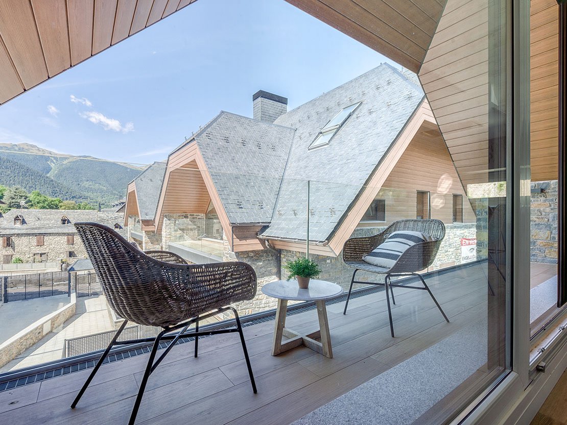 Balcón de Residencial Els Pletieus con sillones de mimbre, vistas a los tejados geométricos de pizarra y las montañas del Valle de Arán