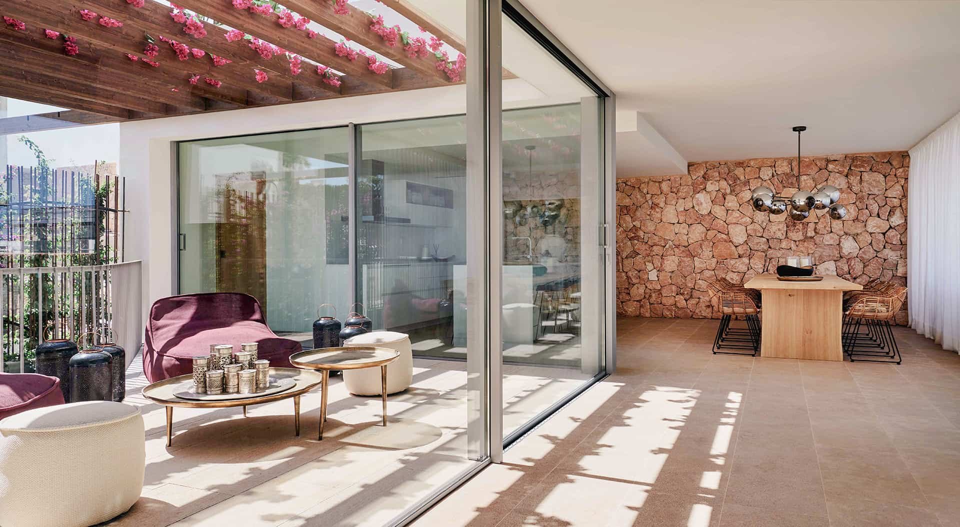 Terraza de Cala Comte con pérgola de buganvilla, pared de piedra vista y grandes puertas correderas de cristal