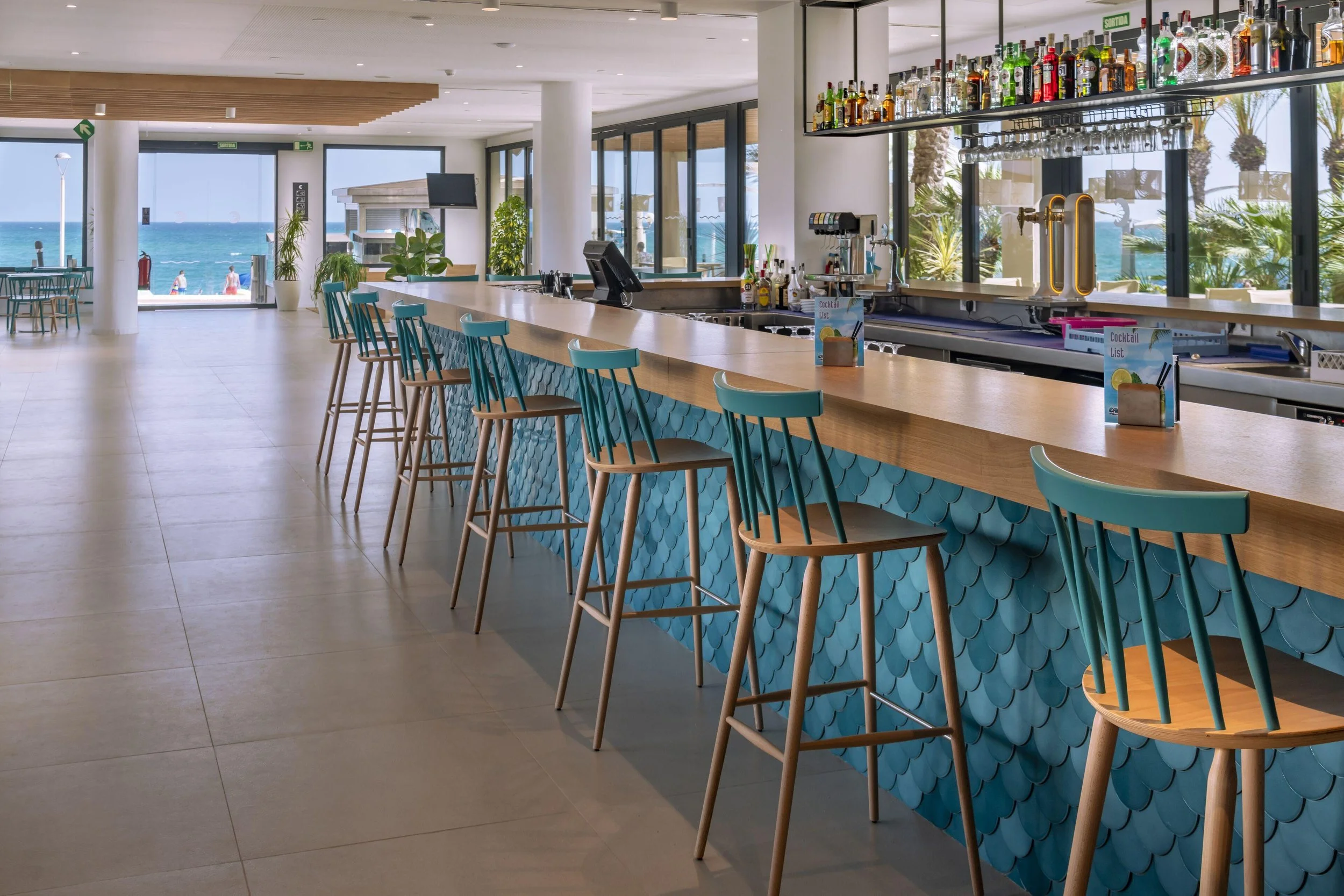 Barra de cócteles de Caprici Beach Hotel & Spa con revestimiento de azulejos azules en forma de escama y vistas al mar