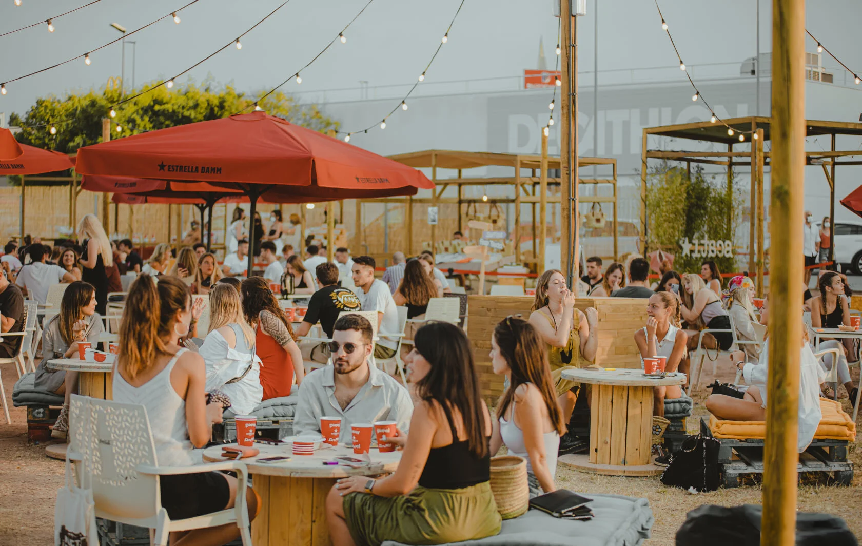 Ambiente social en la terraza exterior de Itaca Market, con mesas de madera, guirnaldas de luces y sombrillas al atardecer