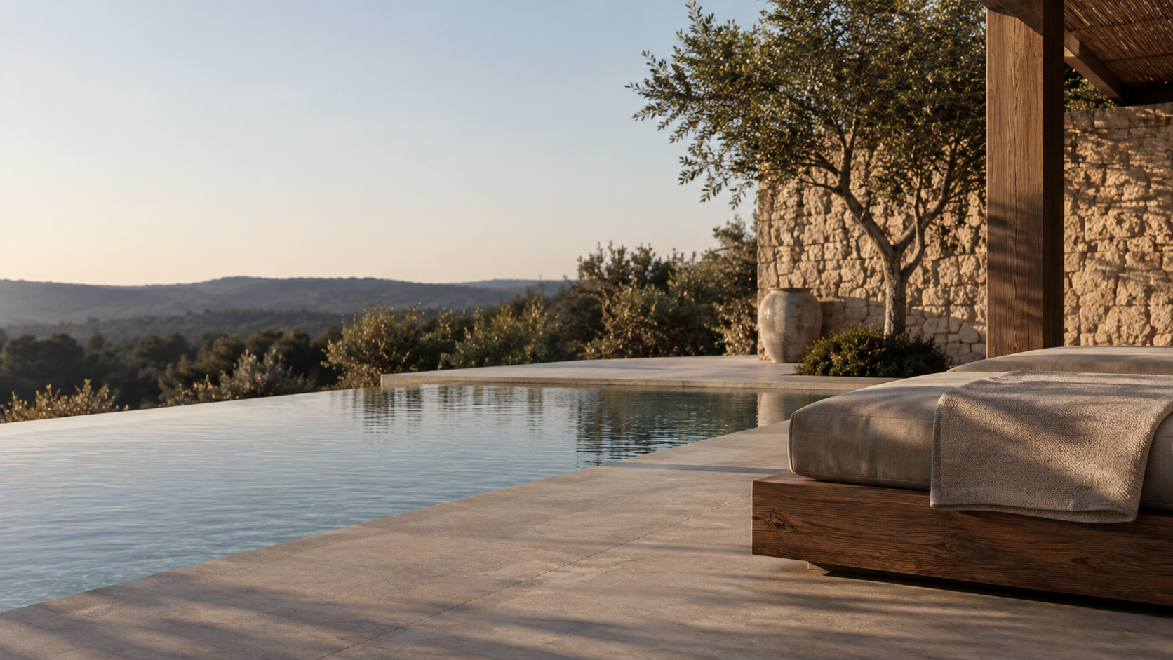 Piscina infinita con terraza de piedra natural, tumbonas y olivo — solución de exteriores ZONA en Cataluña