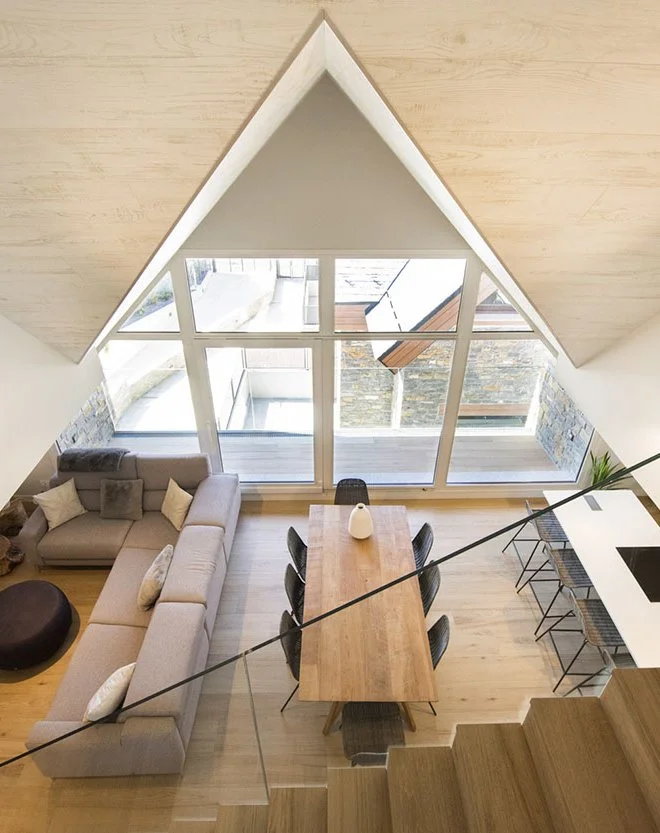 Vista elevada del salón, comedor y cocina de Residencial Els Pletieus, con gran ventanal triangular y estructura de madera vista