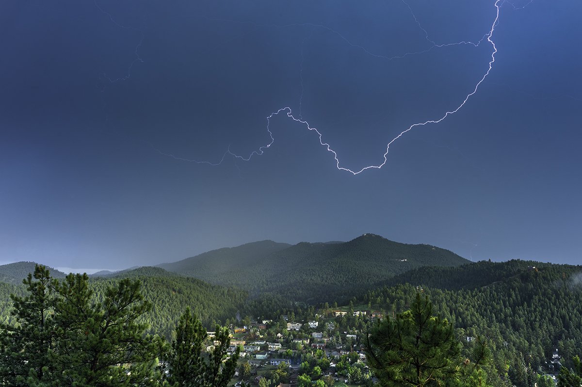 Lightning storm over a mountainous forested landscape with a small town in the valley.