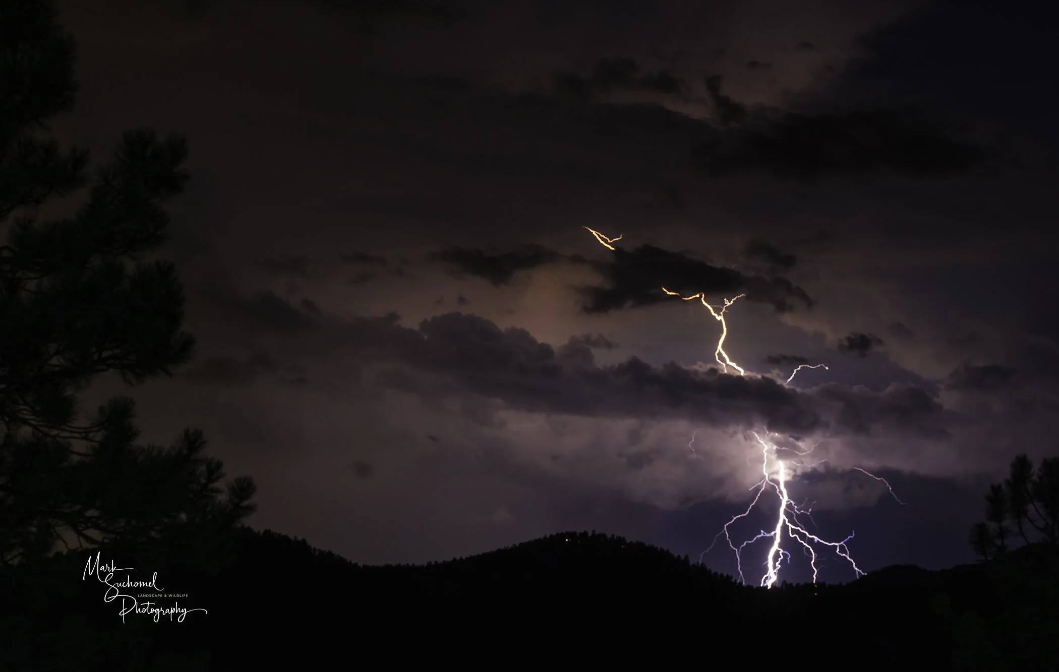 Lightning storm over dark clouds and mountain silhouette at night.