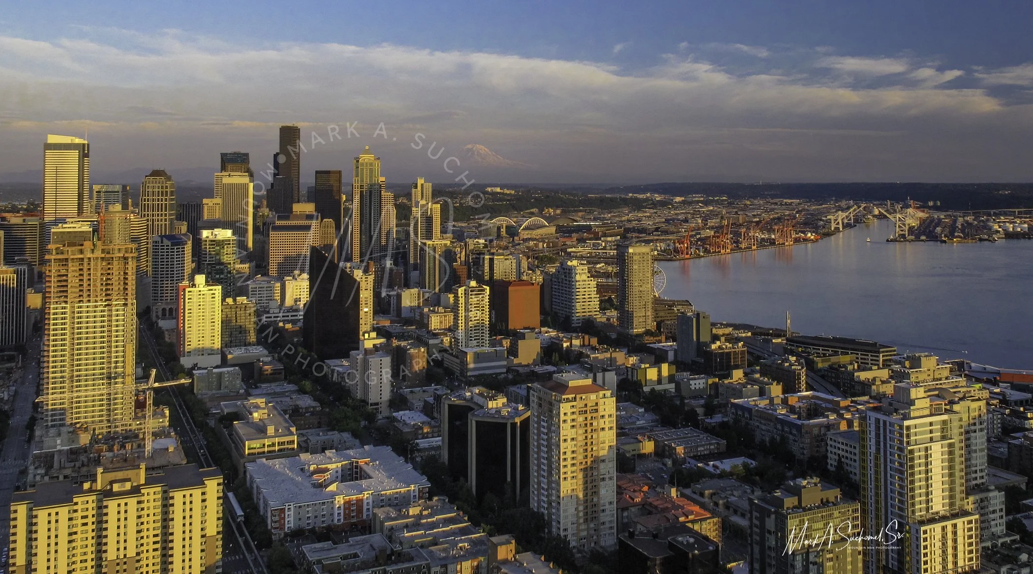 Aerial view of Seattle's downtown skyline, Puget Sound, and Mount Rainier in the background, during sunset.