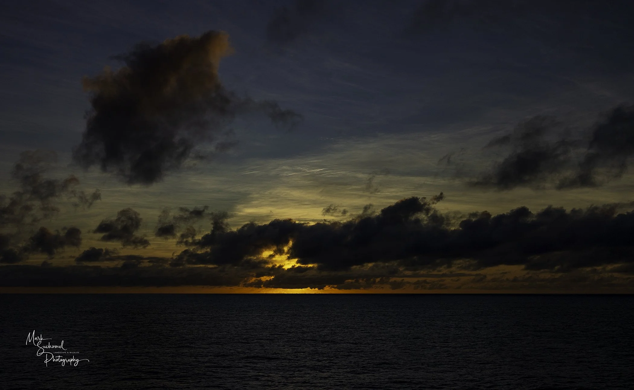 Sunset over the ocean with dark clouds in the sky.