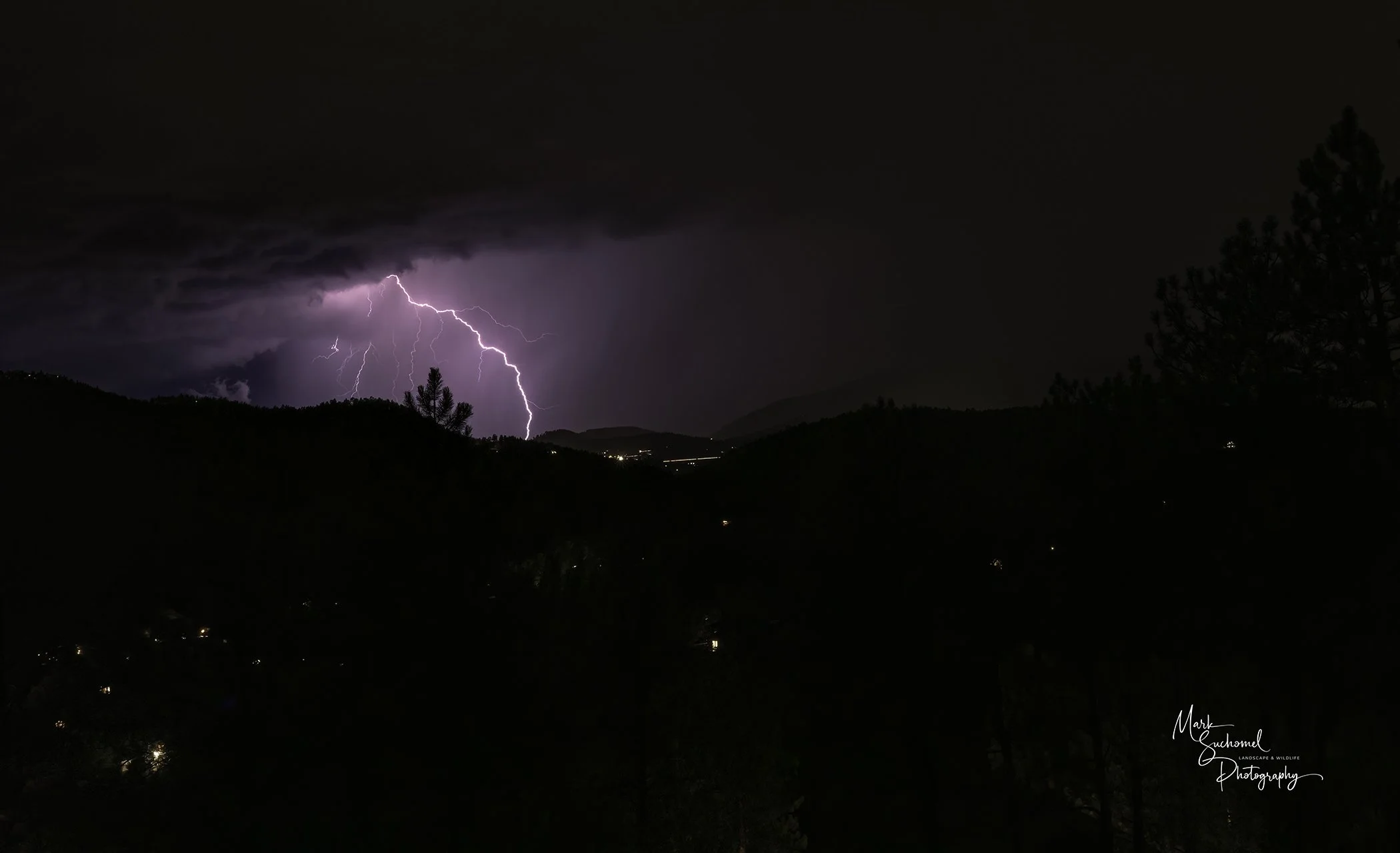 Nighttime scene of a lightning storm over mountains, with dark clouds and lightning strikes illuminating the sky.