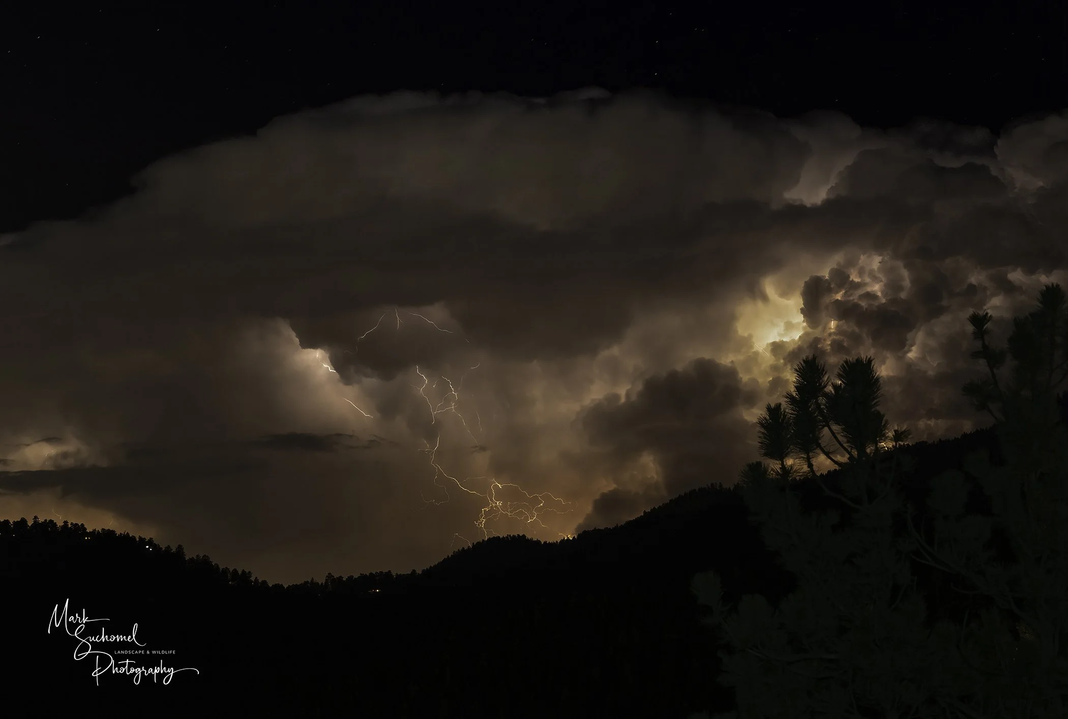 Dark storm clouds with lightning over mountainous landscape at night.