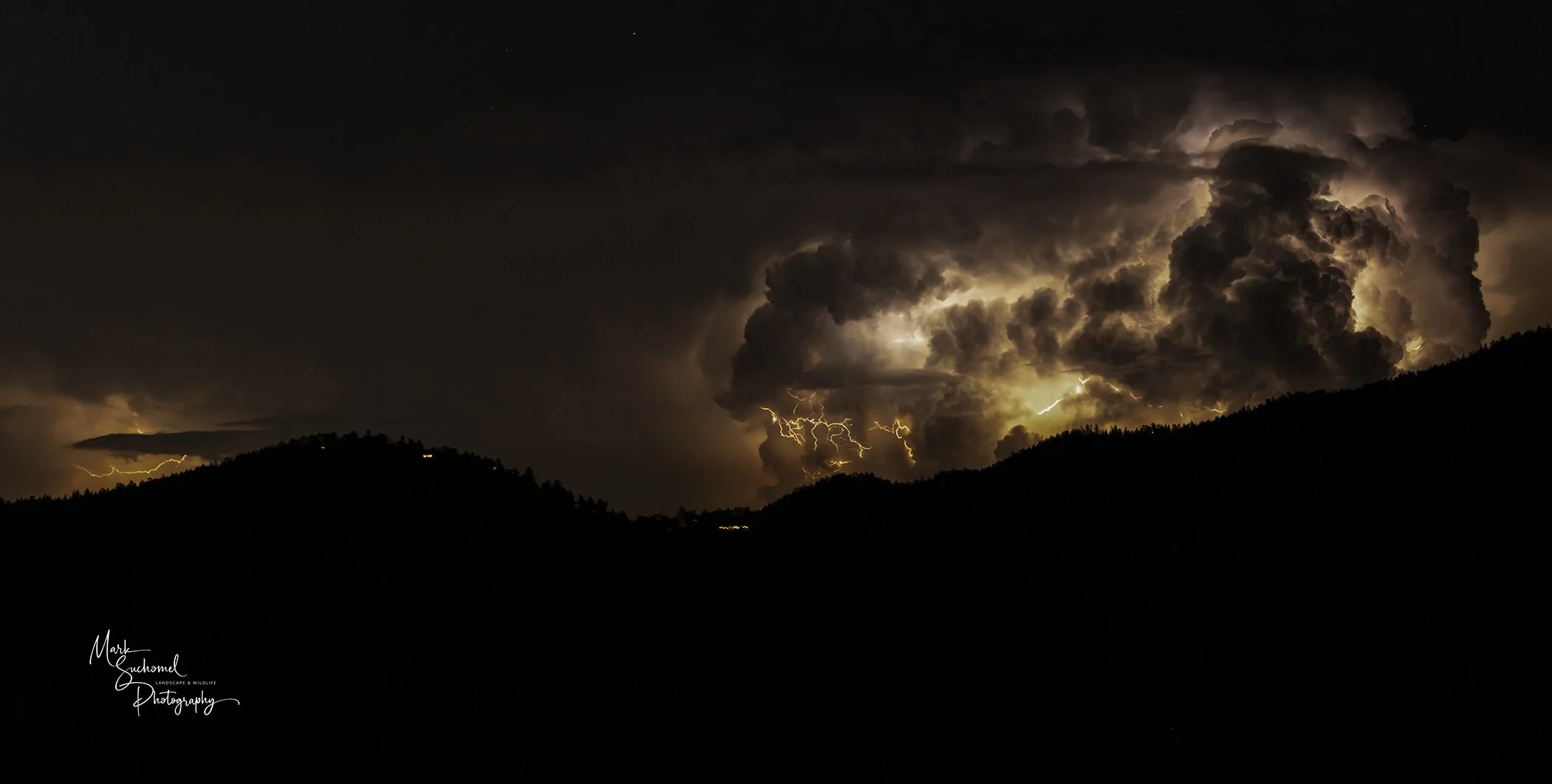 Dark stormy night over mountains with lightning illuminating large cumulonimbus clouds.