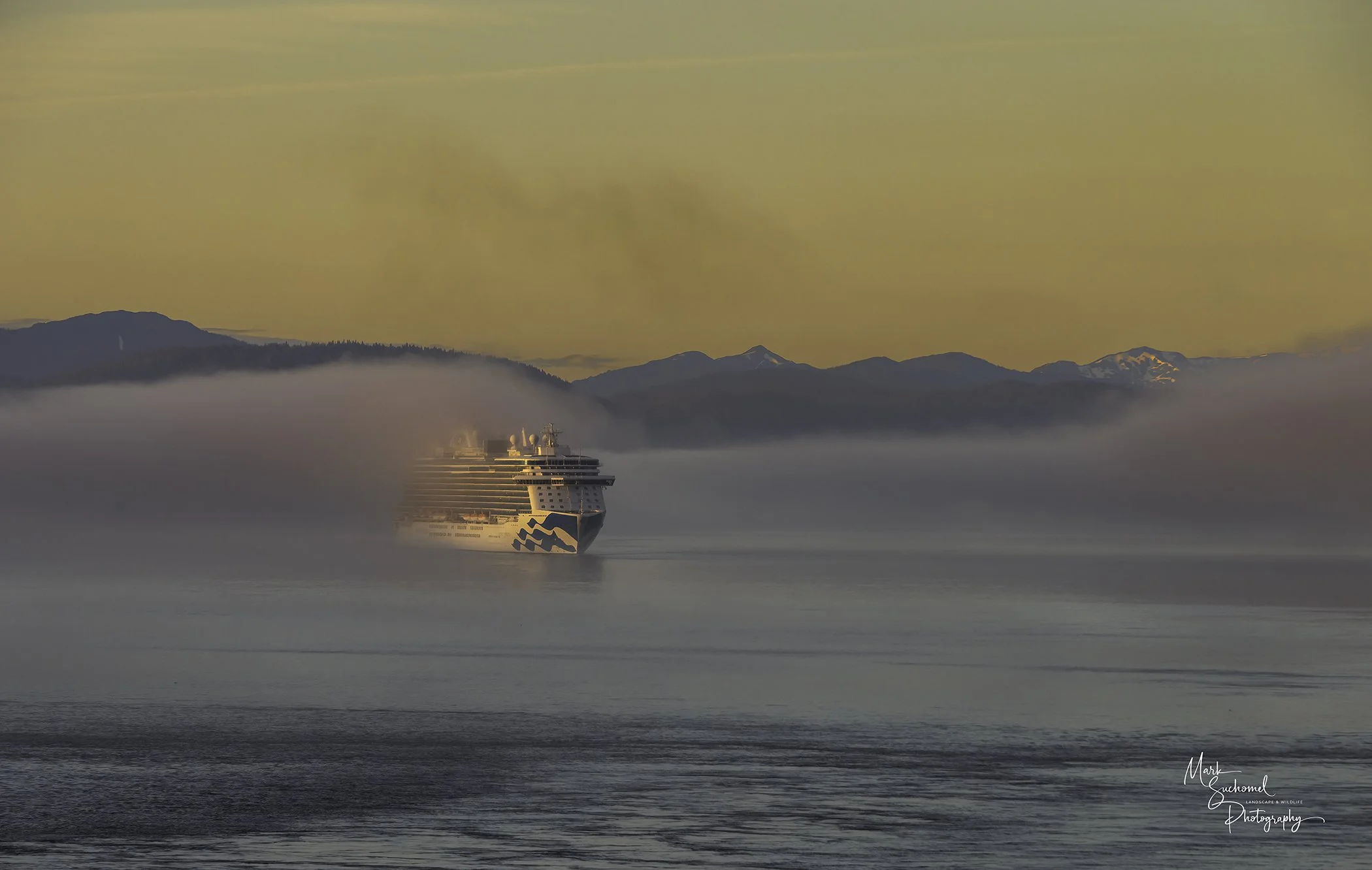A cruise ship sailing through foggy waters with mountain ranges in the background and a colorful sky overhead.