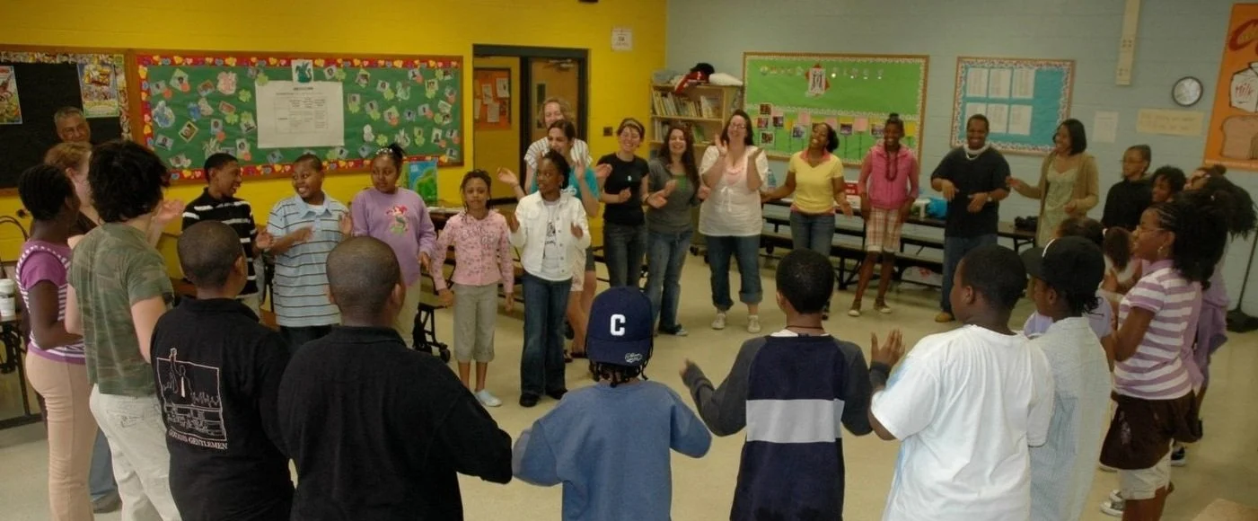 large group of teachers and students dancing in a circle in the cafeteria