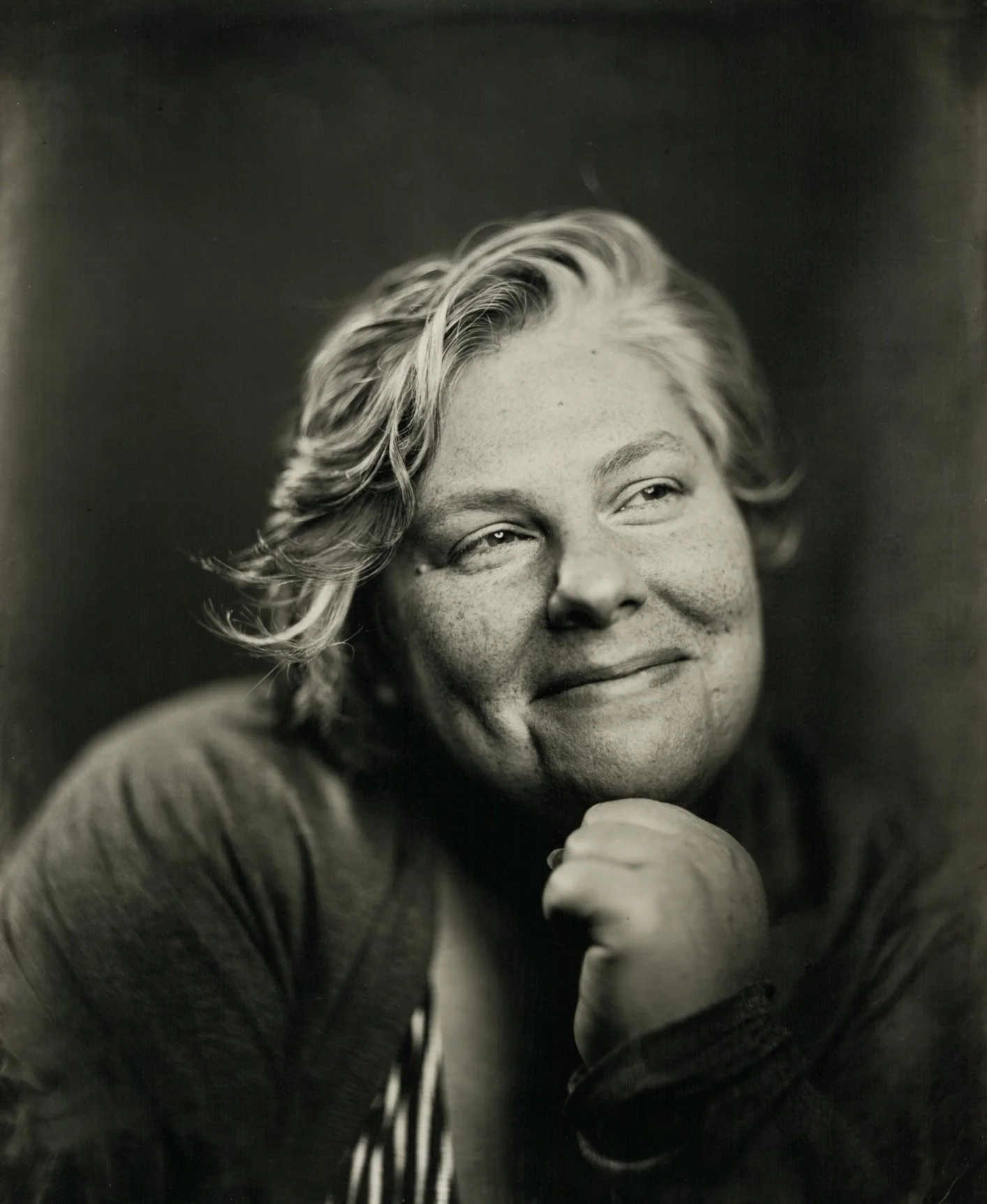 tin type image of woman with short hair and striped shirt smiling with her hand on her chin