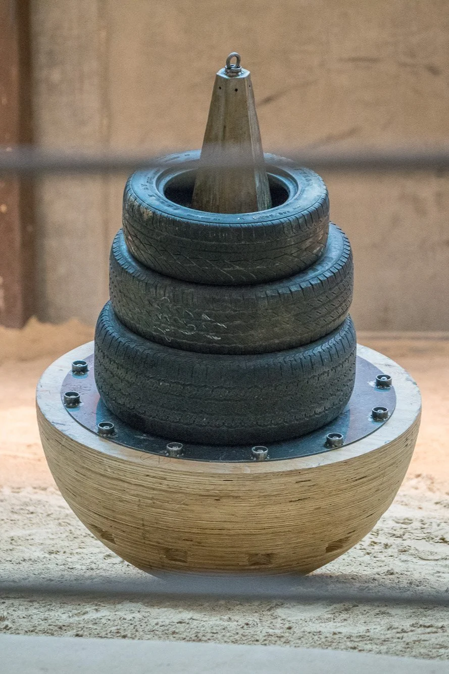 a toy built for elephants that includes a wooden hemisphere base, steel cone topper, and stacking tires.