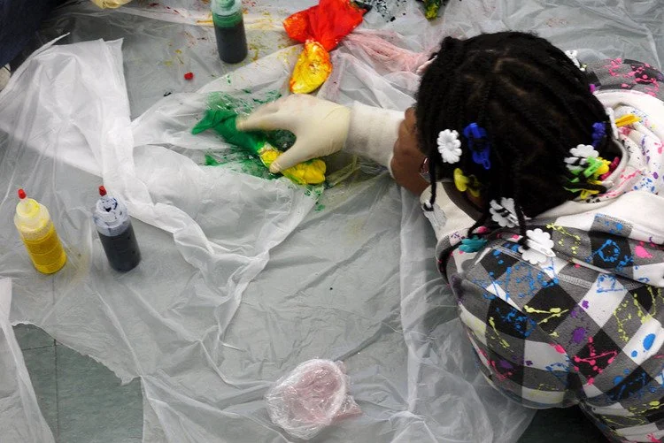 young girl wearing gloves uses fabric dye to paint a shirt