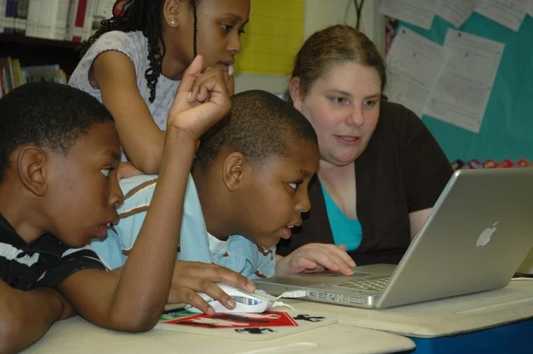 teacher and students gathered in front of laptop