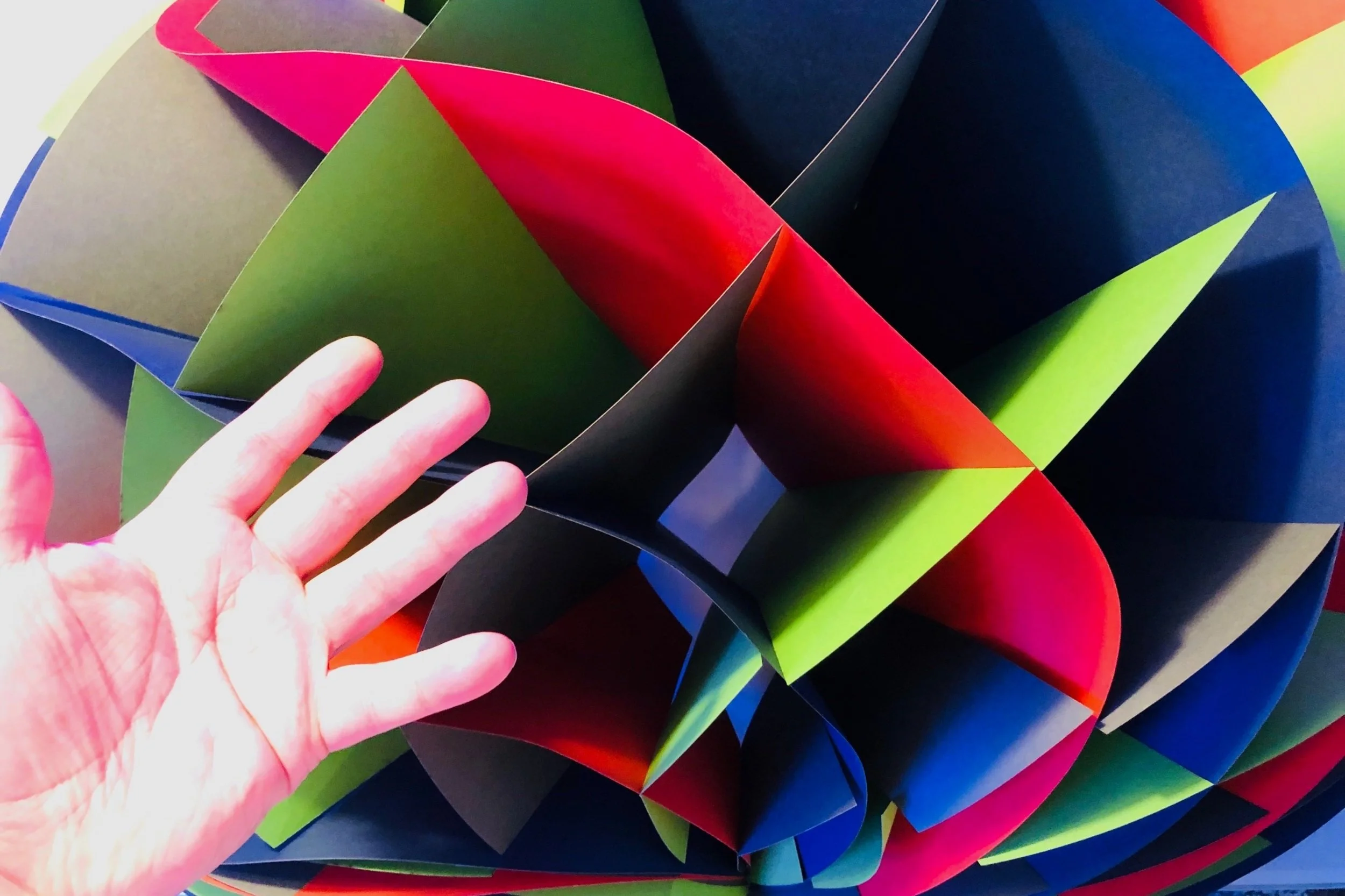 a very large woven paper torus that is collapsing due to heavy weight; hand in front shown for scale