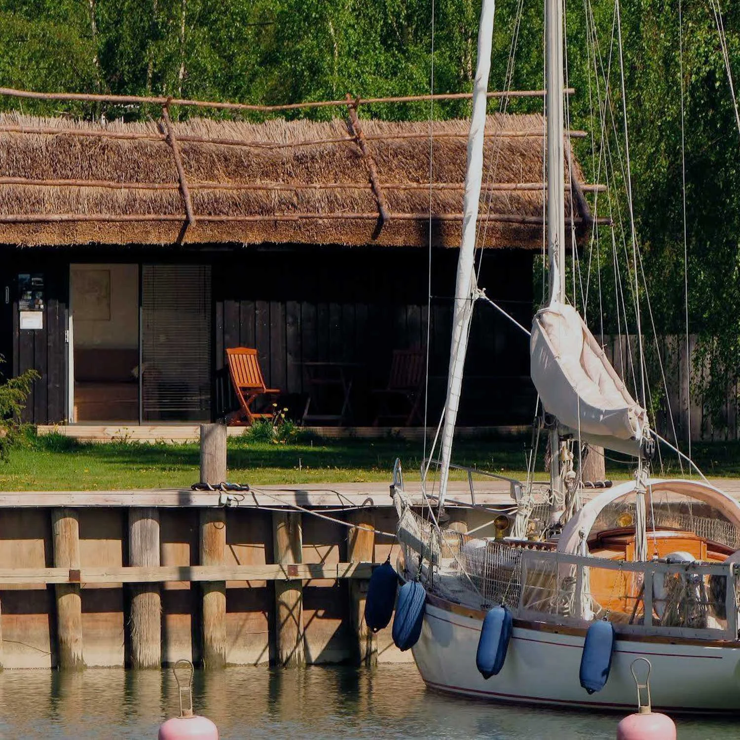 Purjevene satamassa lähellä perinteistä katettua rakennusta vehreässä ympäristössä.