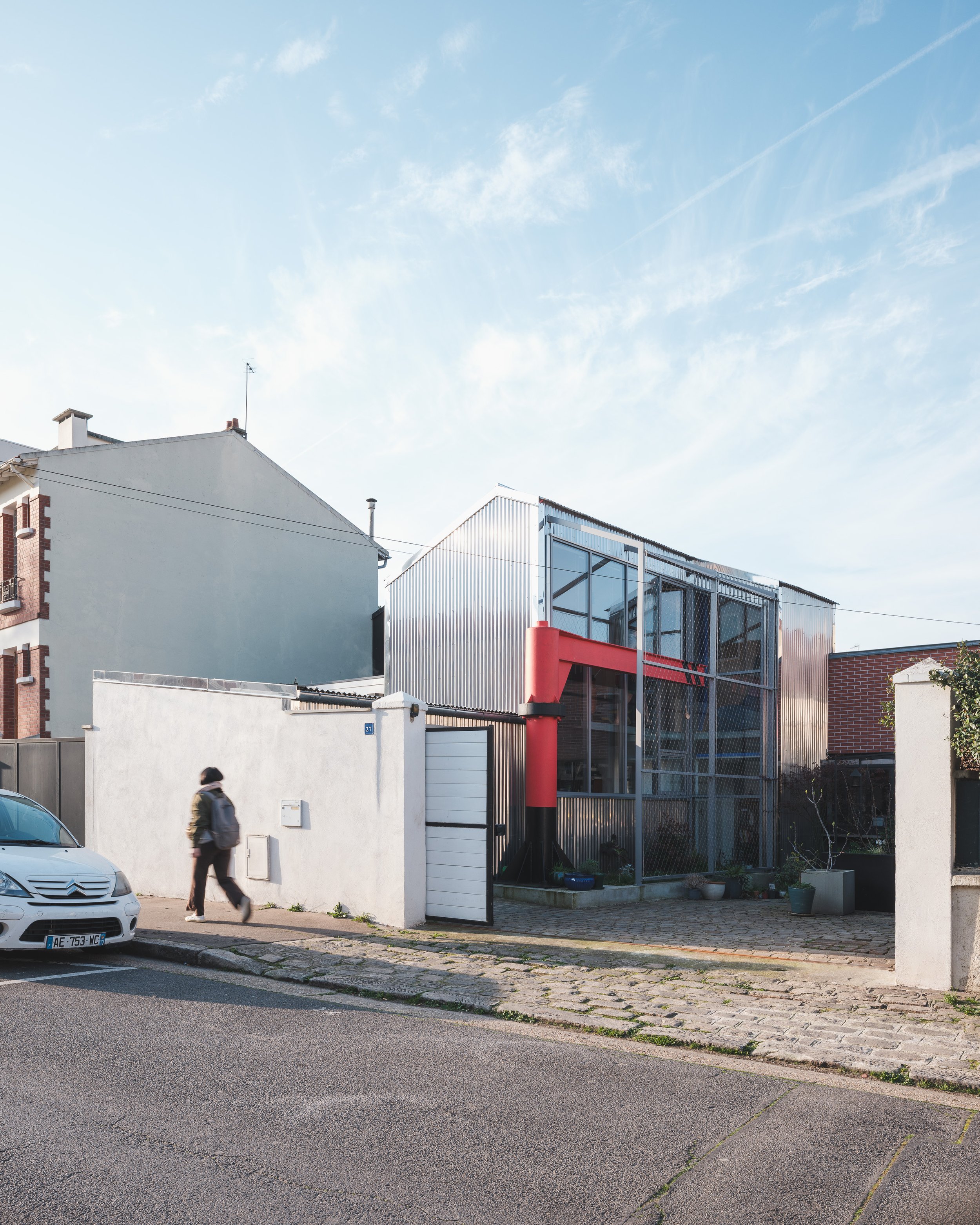Bâtiment contemporain de PC2A à Asnières, avec façade vitrée, panneaux rouges et silhouette d’un passant.