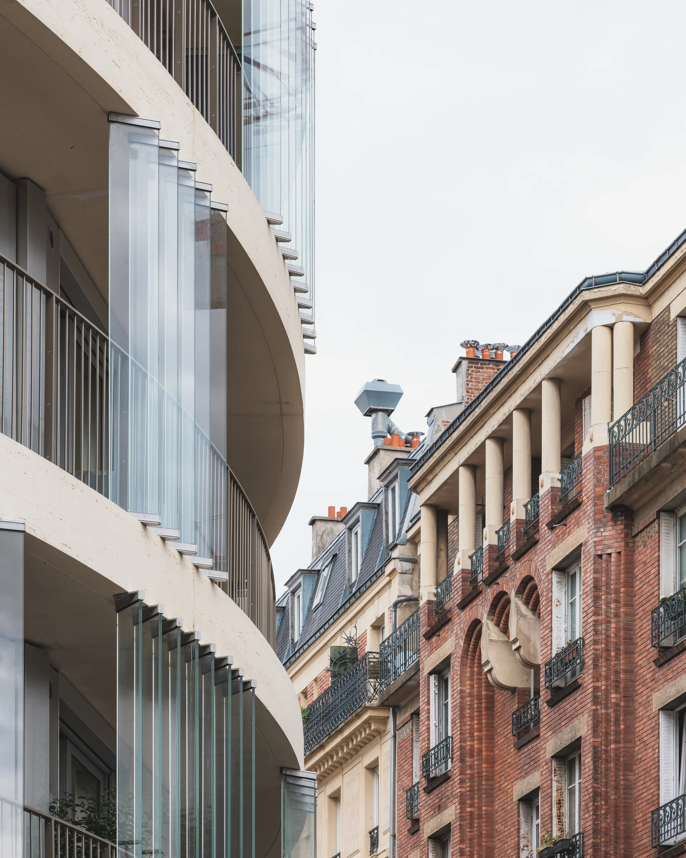 Façade contemporaine aux lignes courbes et balcons vitrés, dans une rue bordée d’immeubles anciens.
