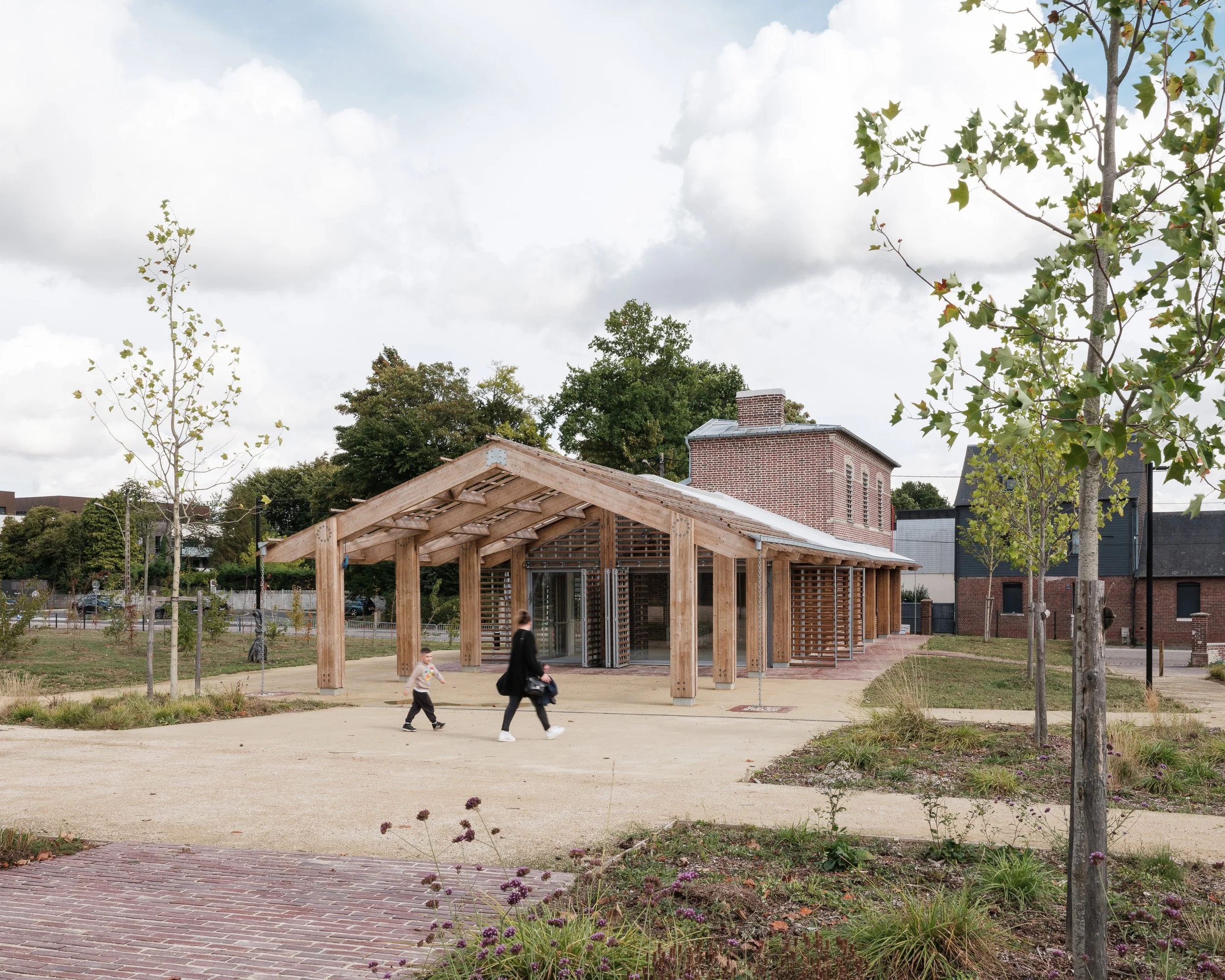 Pavillon en bois aux lignes épurées, entouré de jeunes arbres et d’un sol en gravier.