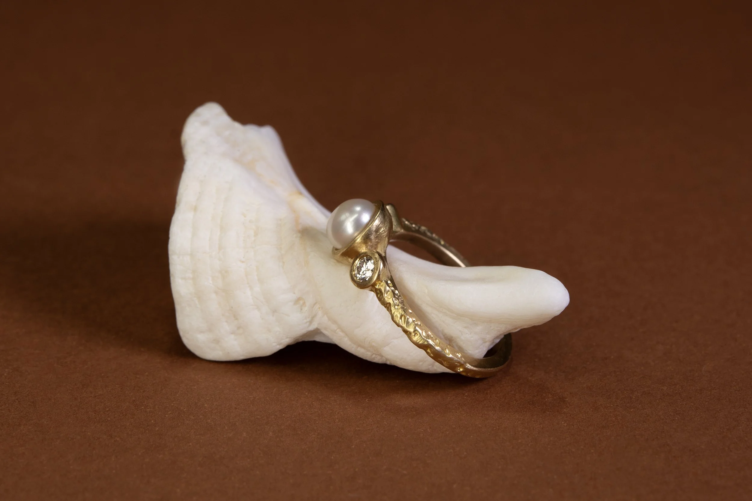 A symbolic and bespoke engagement ring, thoughtfully inspired by the cherished pearl ring once worn by our client's mother. Meticulously handcrafted in luxurious 18kt yellow gold, this meaningful piece is brought to life with intricate elemental text