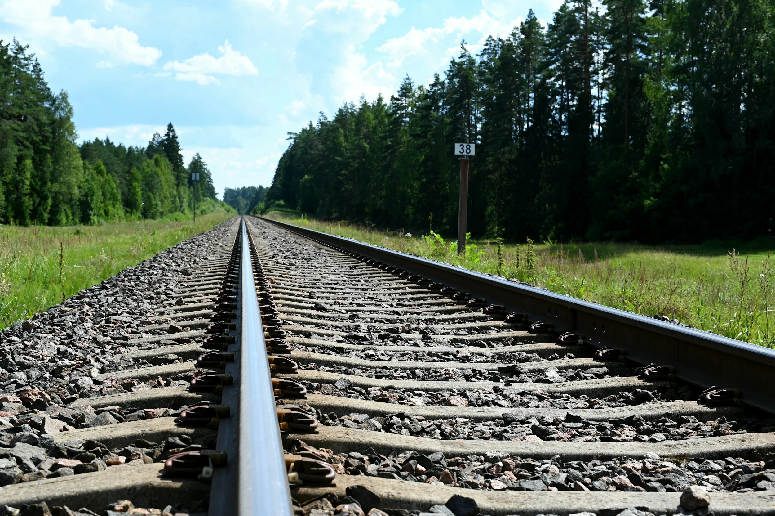Railroad tracks running through a green forest landscape under a partly cloudy sky.