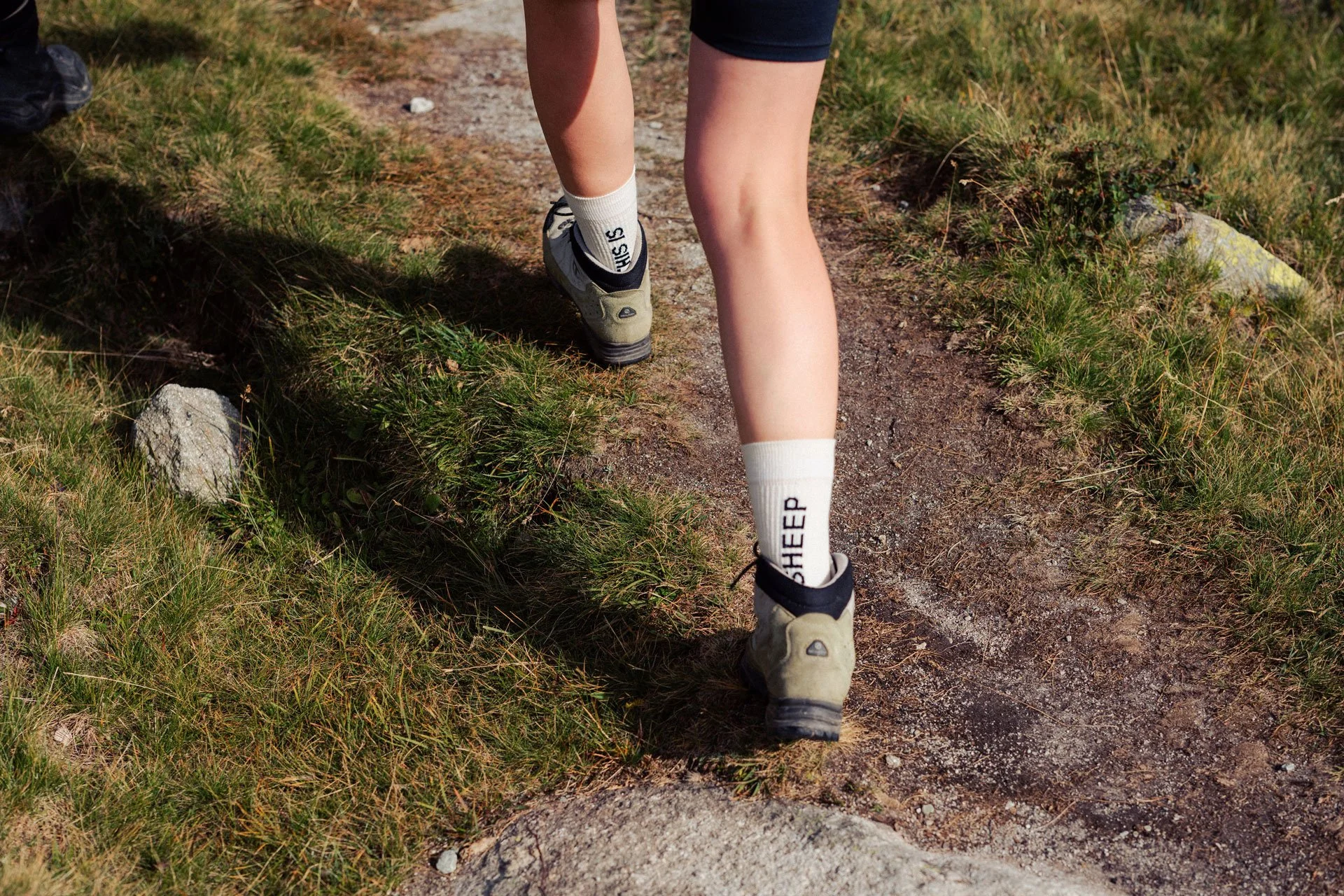 Frau in Wanderschuhen mit weissen «THIS IS SHEEP»-Socken wandert auf Bergweg