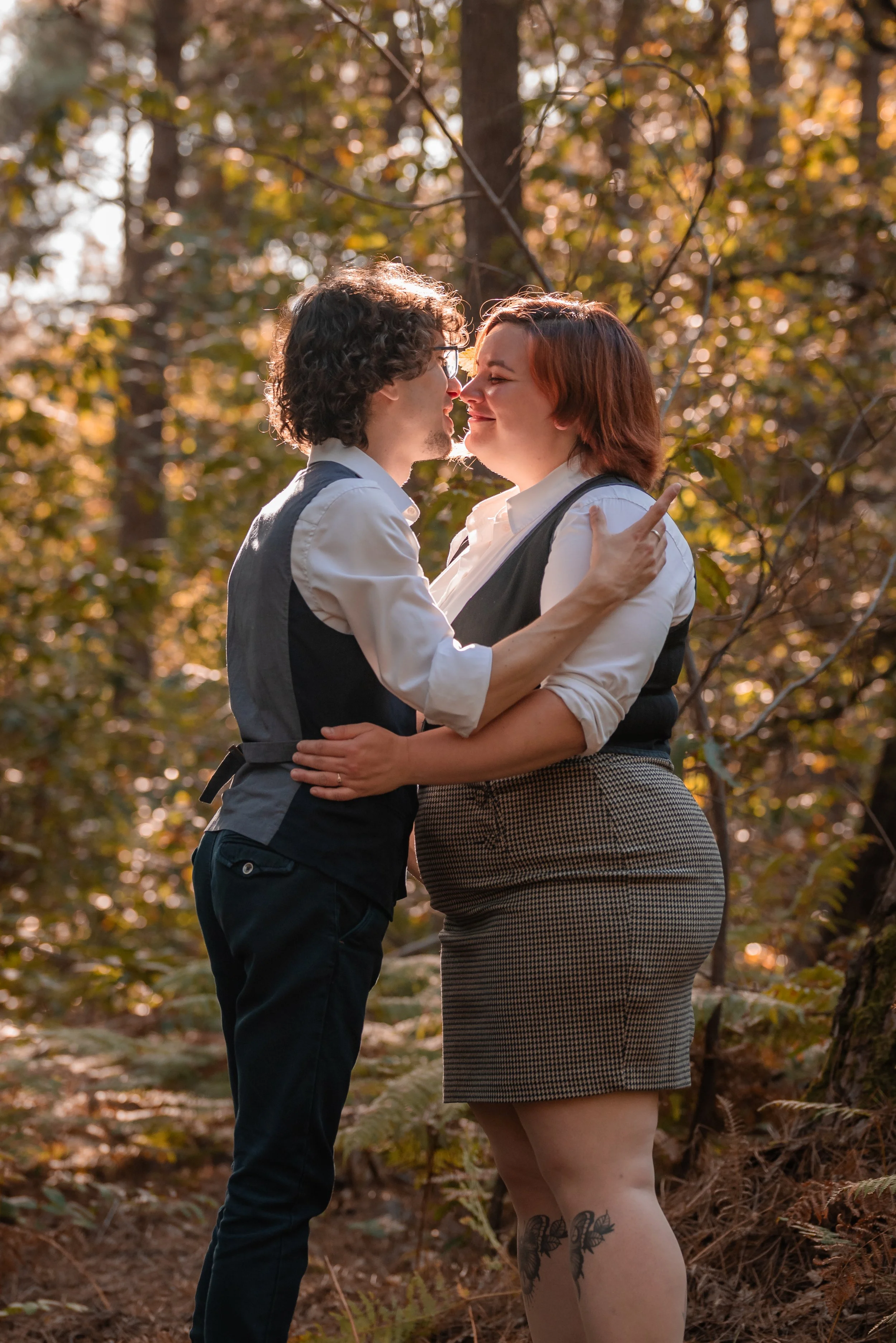 Un couple s'apprête à s'embrasser dans une forêt en automne, avec des feuilles dorées et oranges en arrière-plan.