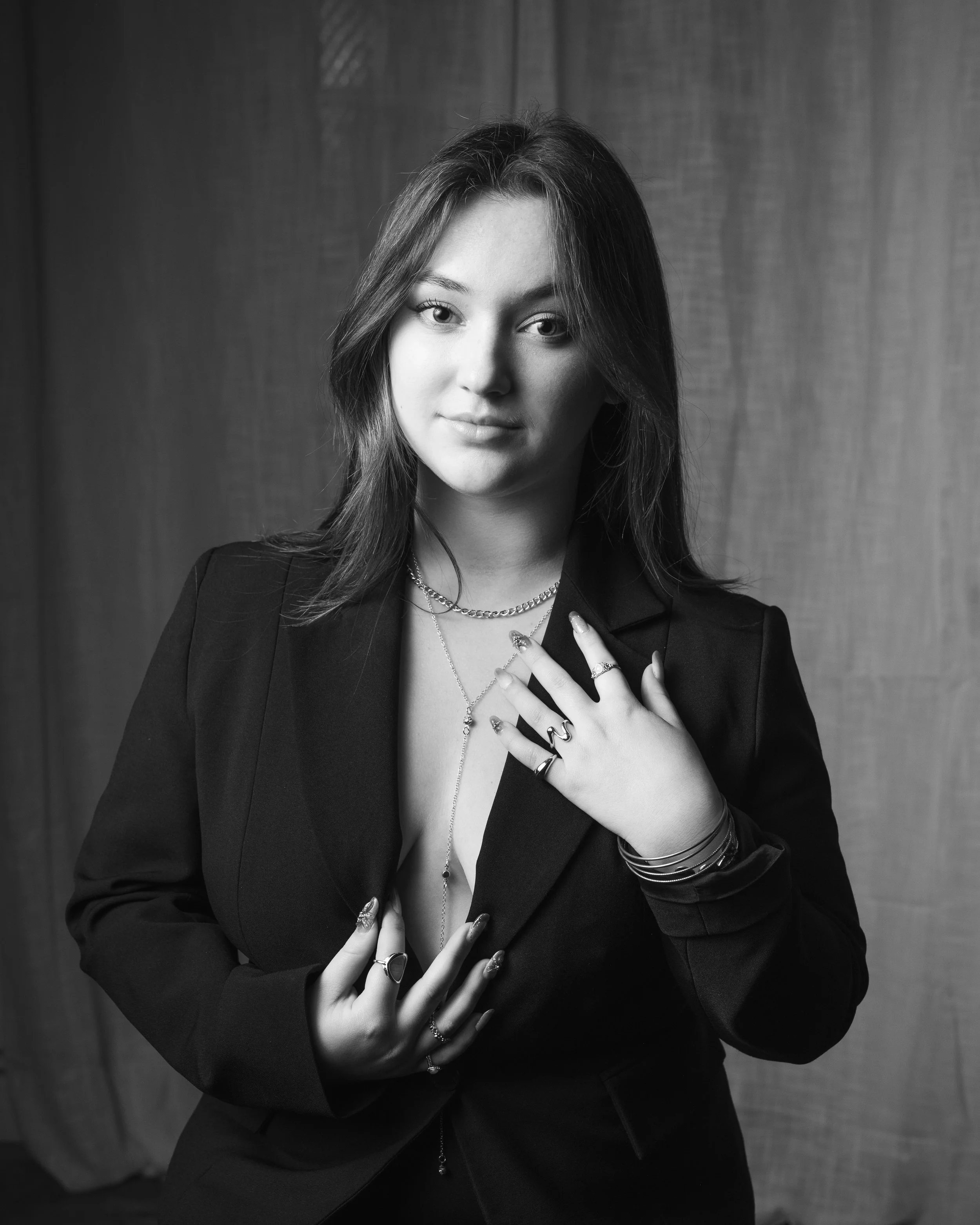 Portrait noir et blanc d'une jeune femme posant avec ses mains sur sa poitrine, portant des bijoux et un blazer