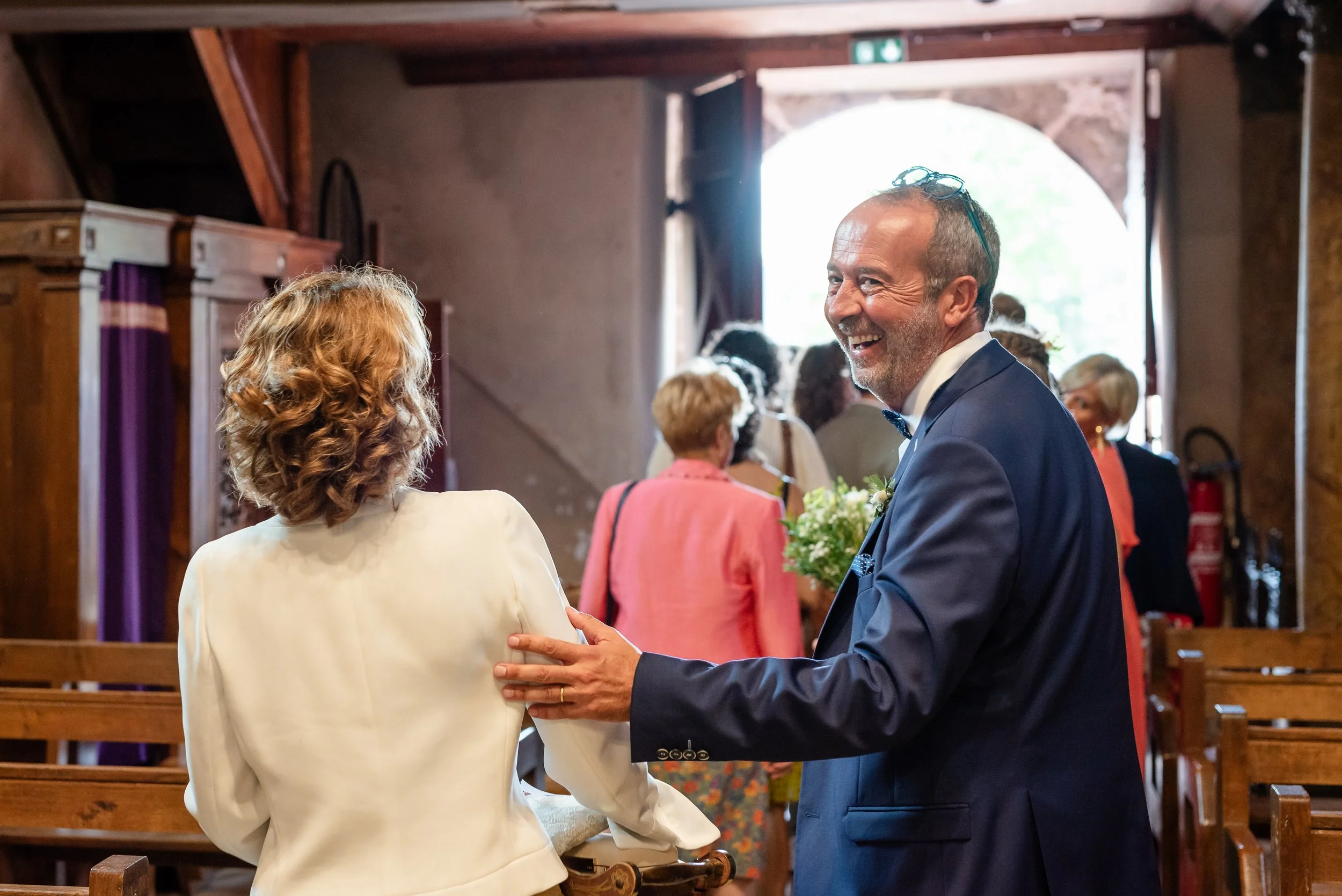 Un homme en costume de mariage souriant en tenant la main d'une femme lors d'une cérémonie dans une église en bois.