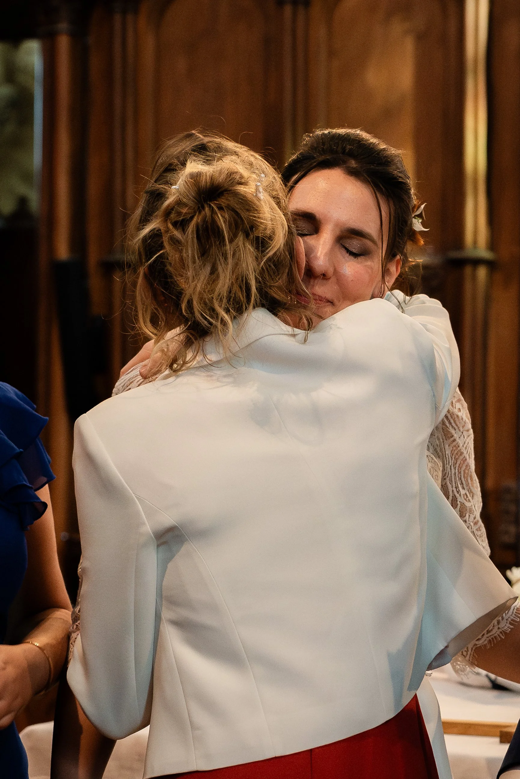 Deux femmes s'embrassent lors d'une cérémonie, l'une portant une robe blanche et l'autre une robe rouge.