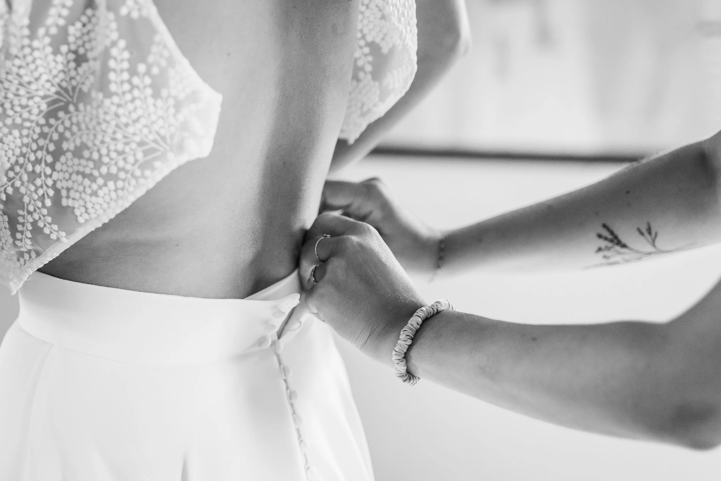 Une personne portant une robe blanche en dentelle ajustée, tenant la main d'une autre personne. La photo est en noir et blanc, montrant un moment intime ou romantique.