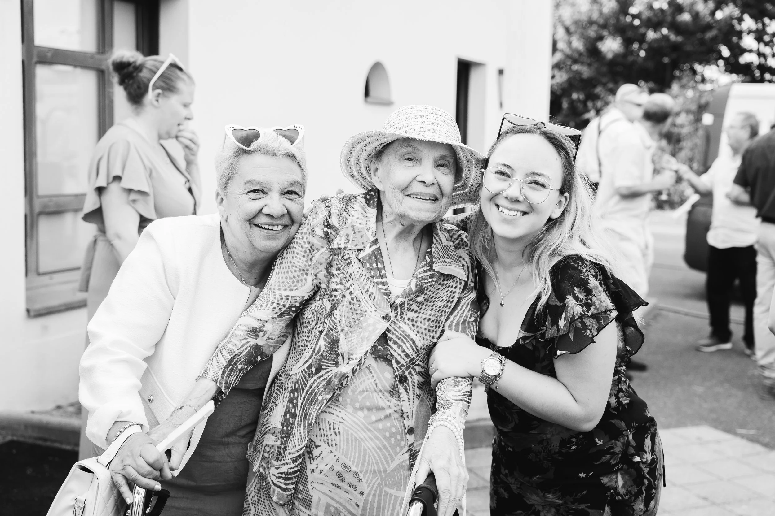 Groupe de quatre femmes âgées souriantes posant ensemble, une d'elles portant un grand chapeau, lors d'un rassemblement extérieur.