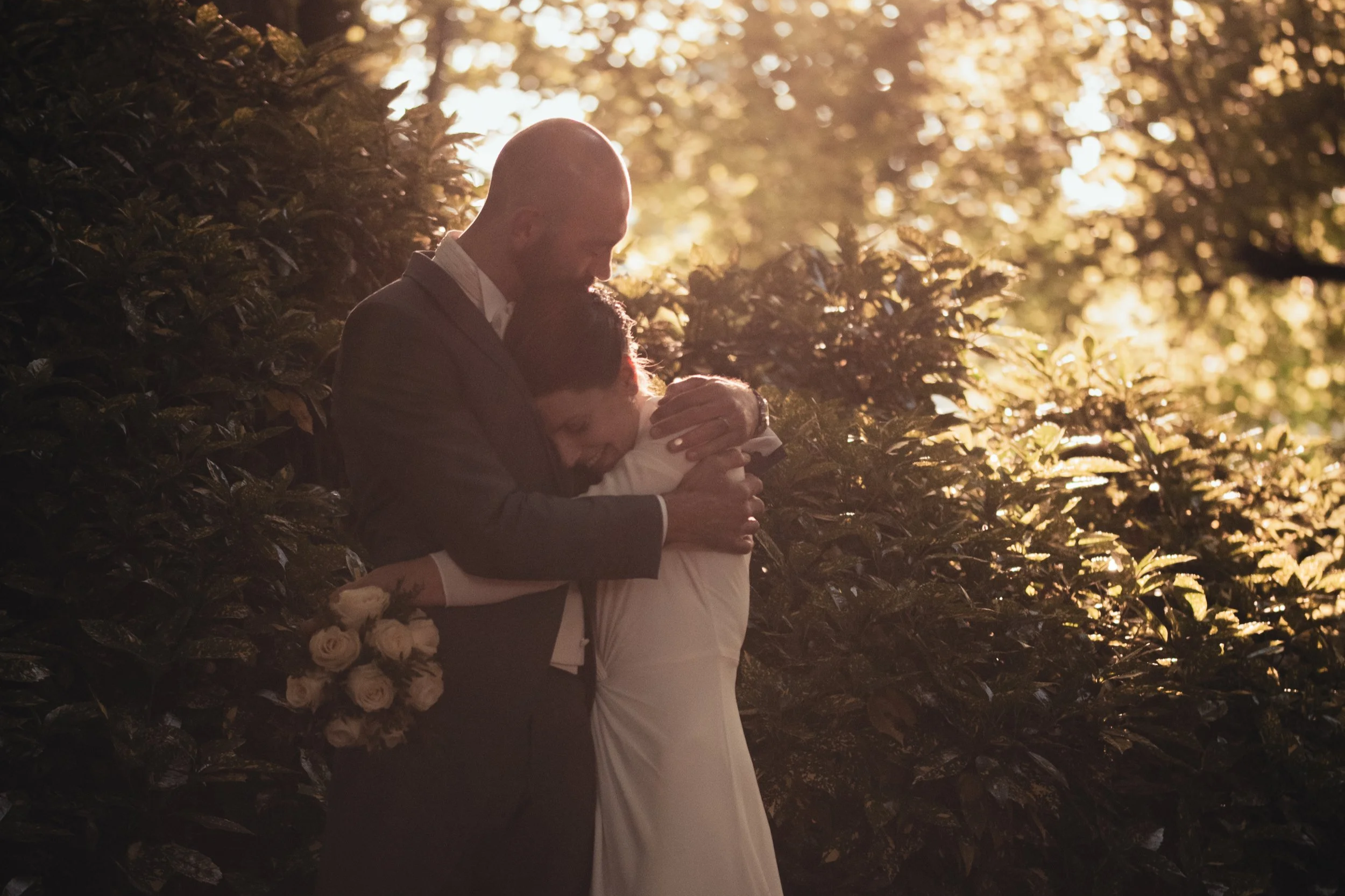 Un couple en tenue de mariage partage un moment d'émotion dans la nature lors d'un coucher de soleil.