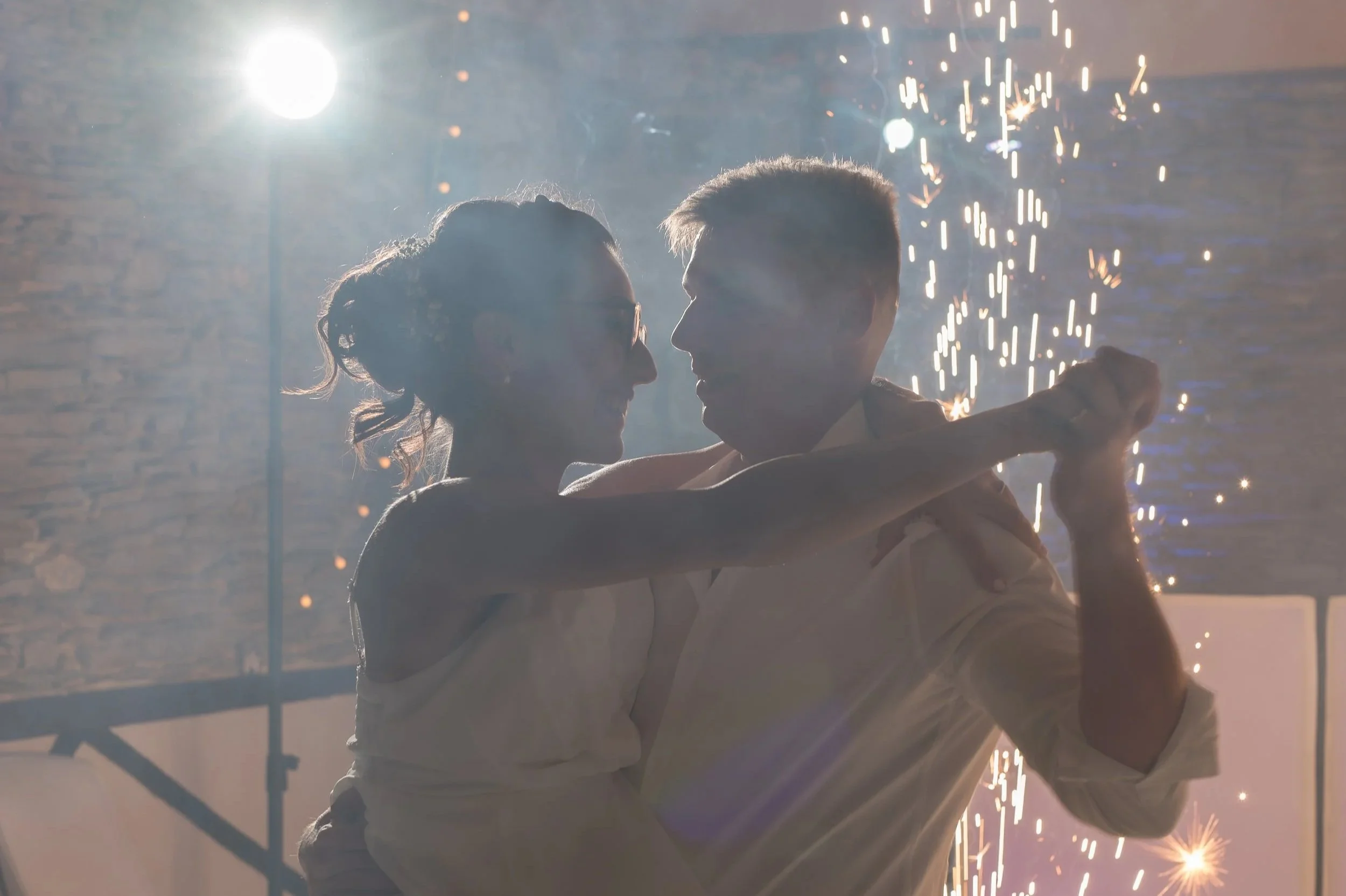 Un couple dansant lors d'une célébration avec des étincelles, silhouette face à face, ambiance festive et chaleureuse.