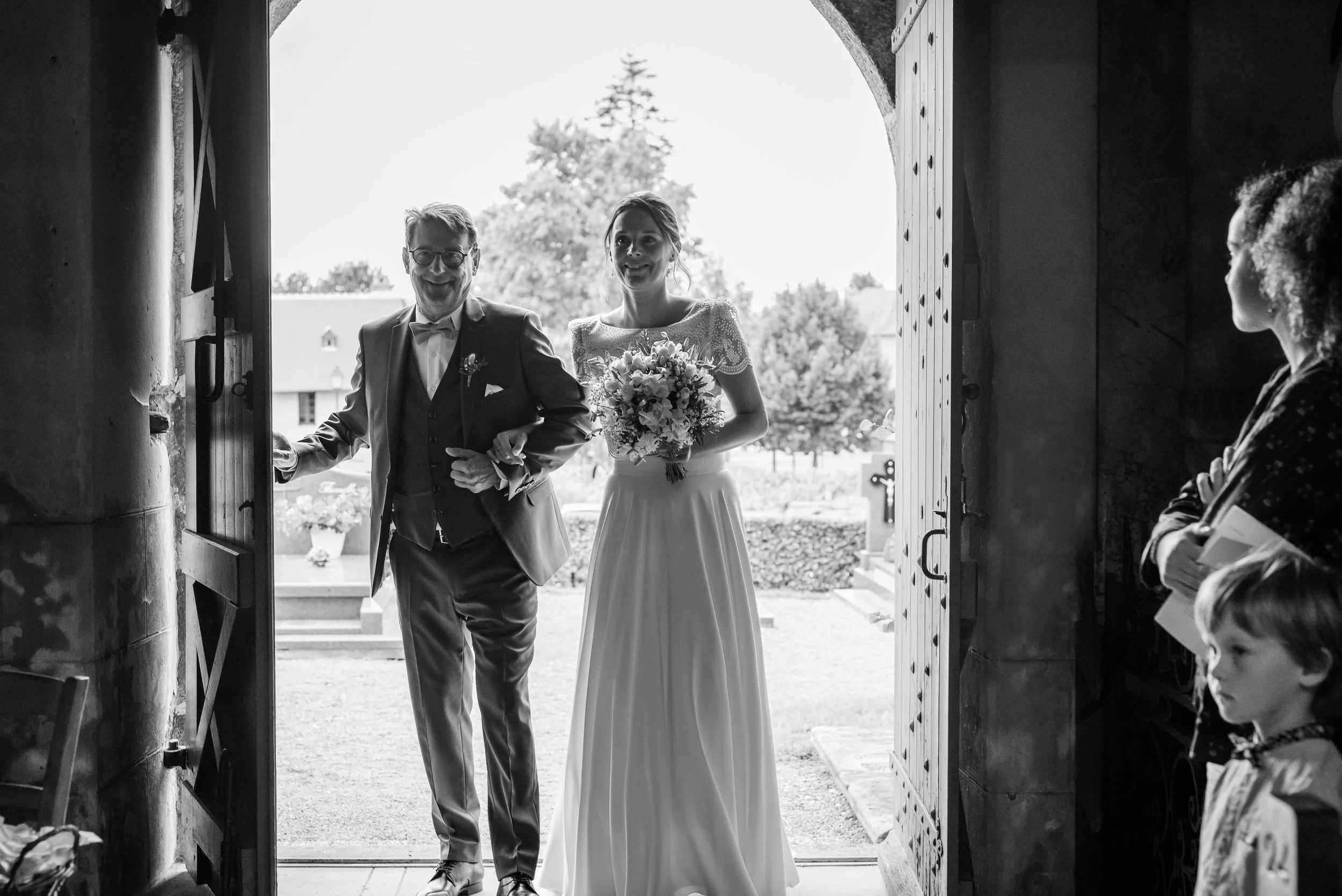 Mariée et homme en costume arrivant dans une église pour un mariage, vue en noir et blanc.
