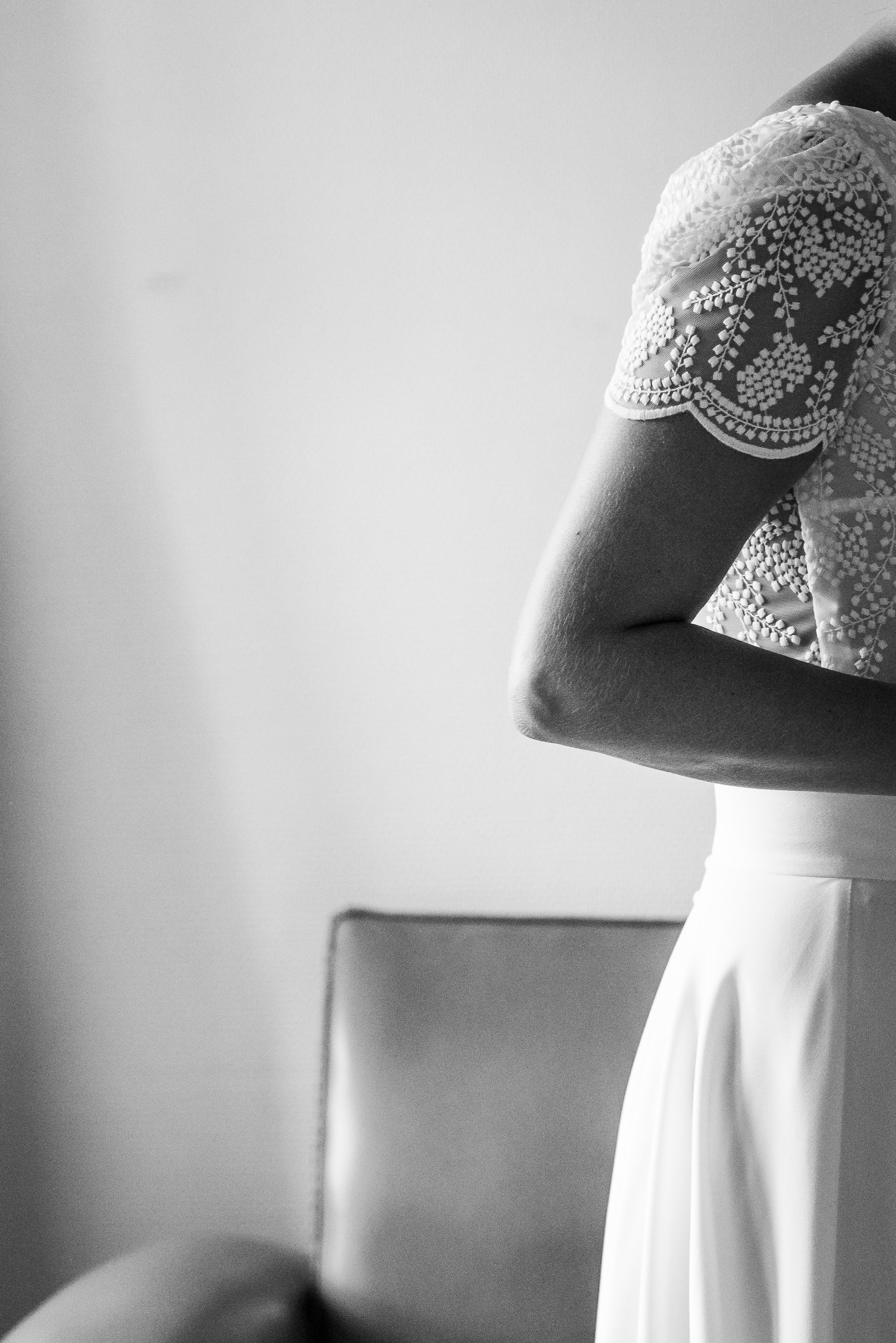 Une femme portant un haut à manches courtes avec broderies de fleurs, vue de côté, dans un intérieur monochrome.