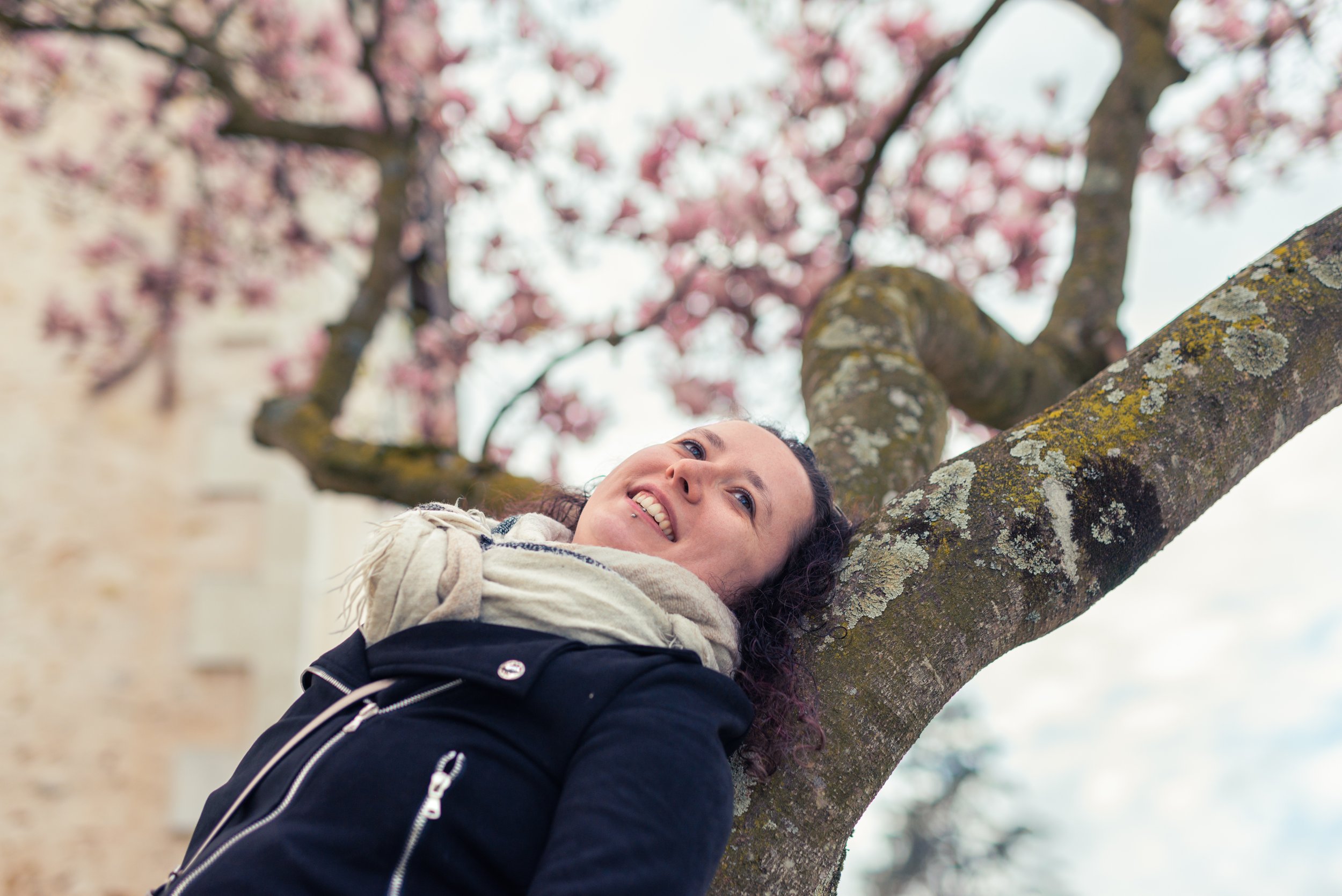 Une femme souriante repose sur une branche d'arbre en fleurs roses.