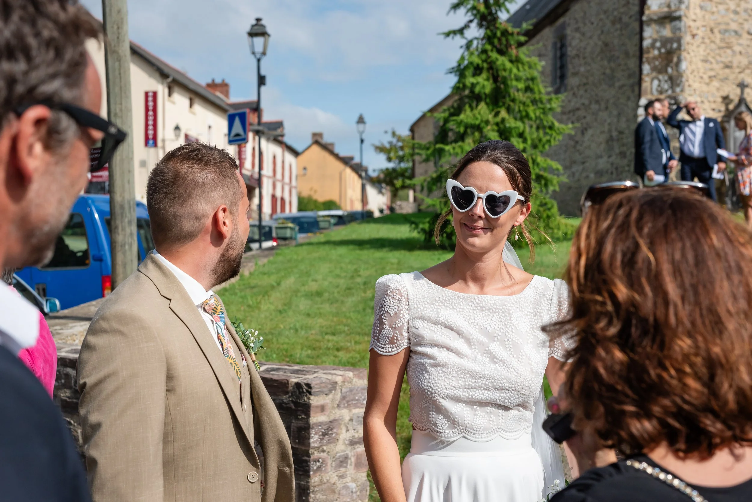 Un groupe de personnes lors d'une cérémonie en plein air, avec une femme portant des lunettes en forme de cœur, au centre.