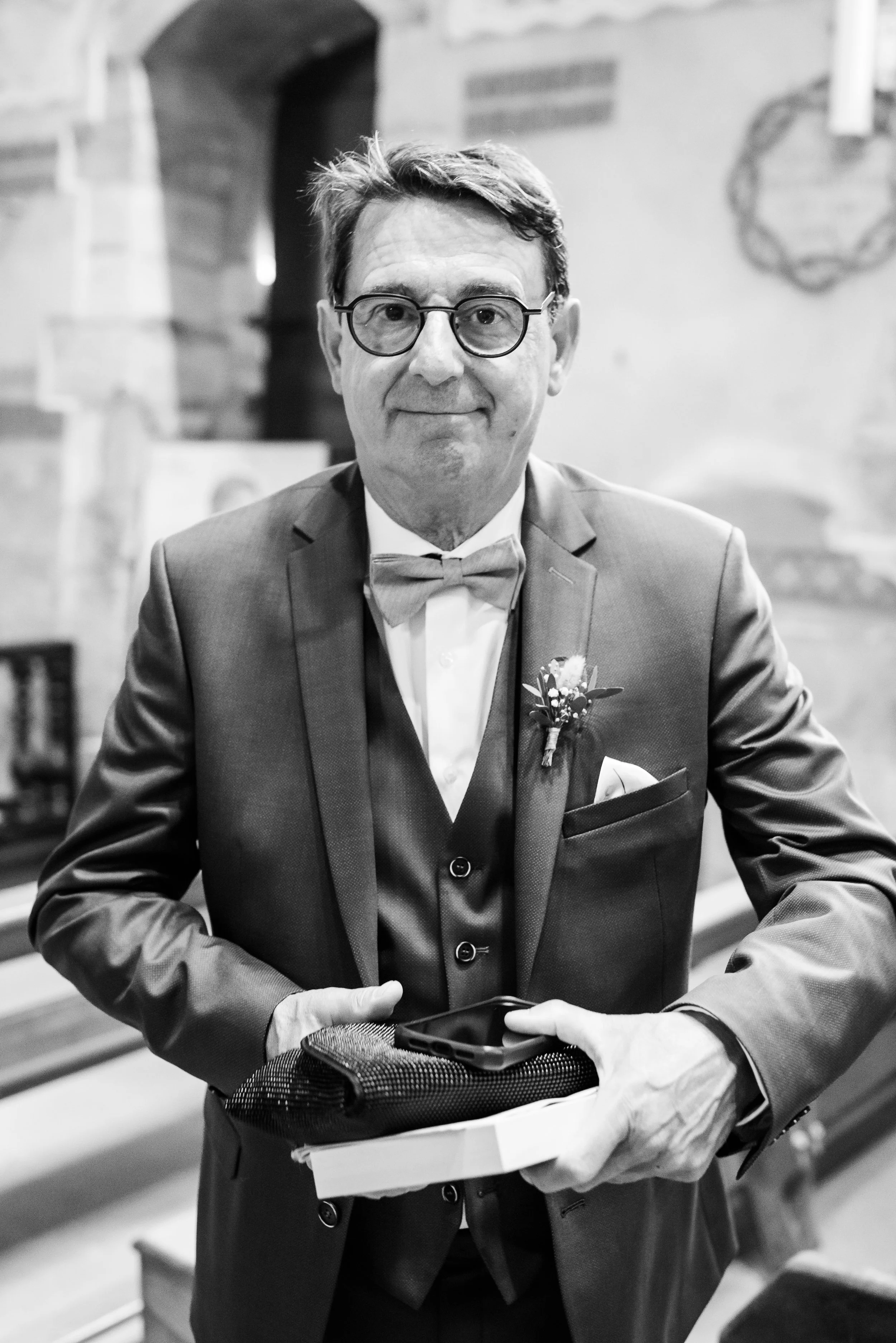 Un homme en costume et lunettes, tenant une boîte avec des mains gantées.