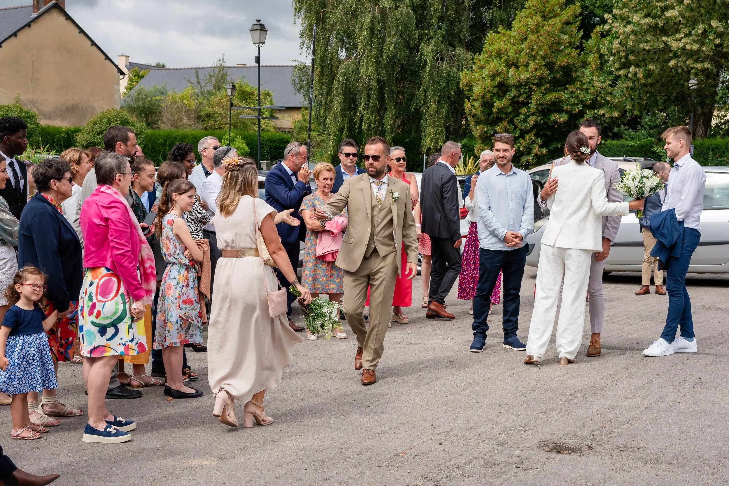 Groupe de personnes lors d'une cérémonie de mariage en plein air, avec le couple de mariés en train de s'embrasser, entourés d'invités élégamment habillés.